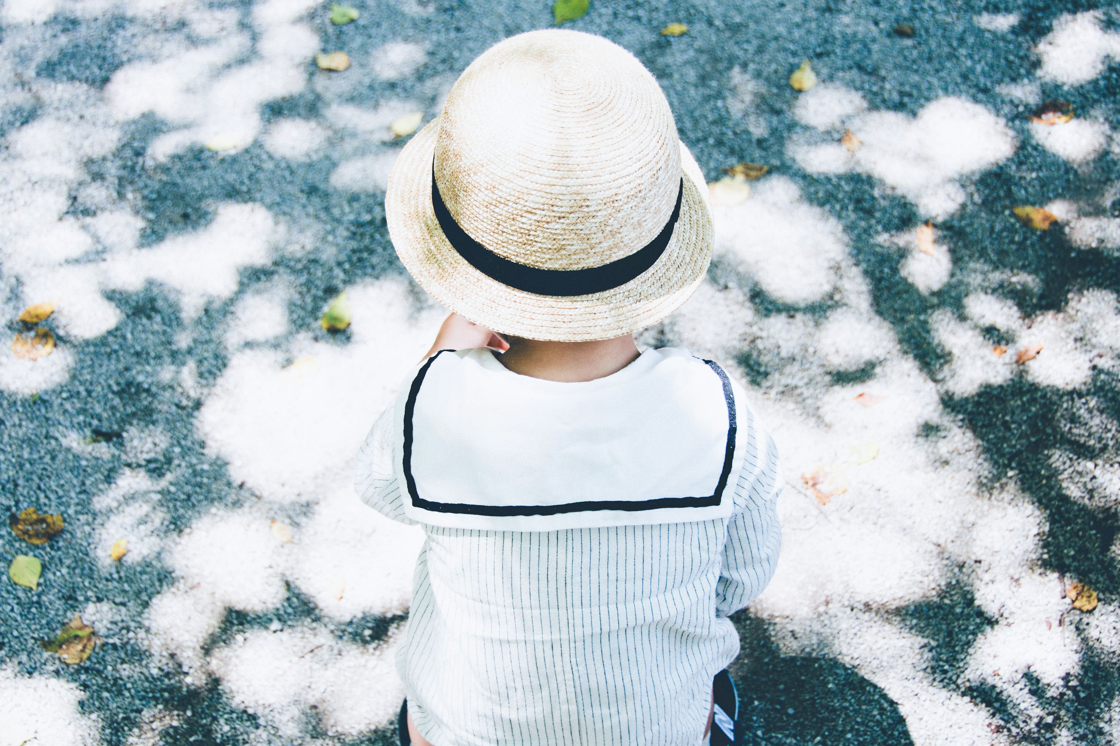 Un bambino con un cappello di paglia seduto su un letto di petali bianchi