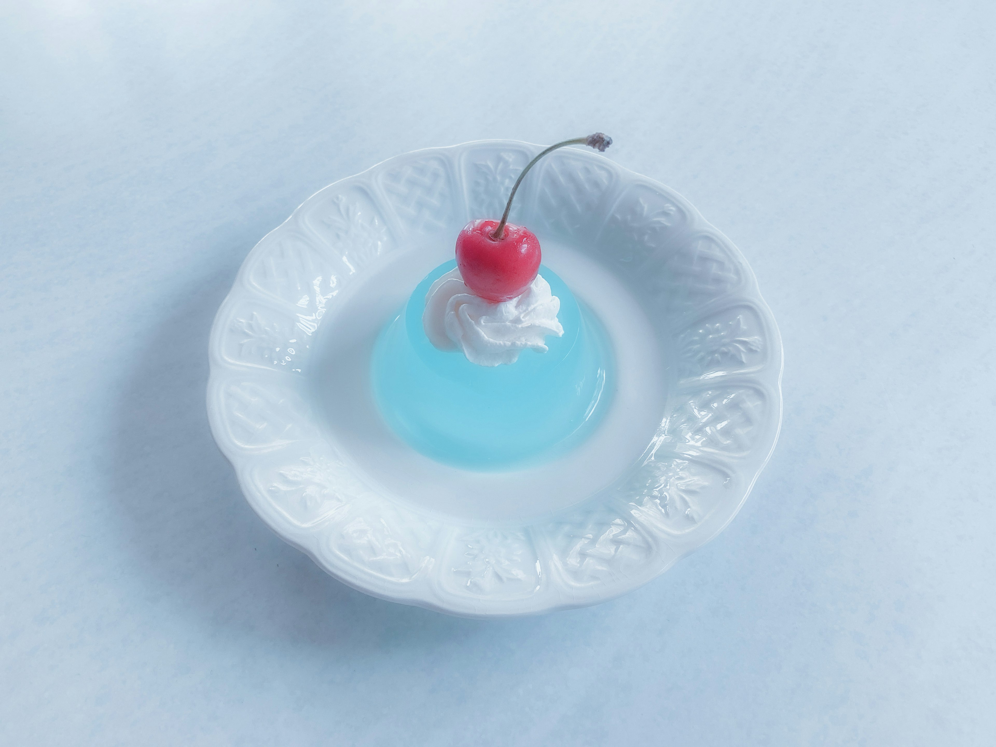 Blue jelly with whipped cream and a red cherry on a white plate