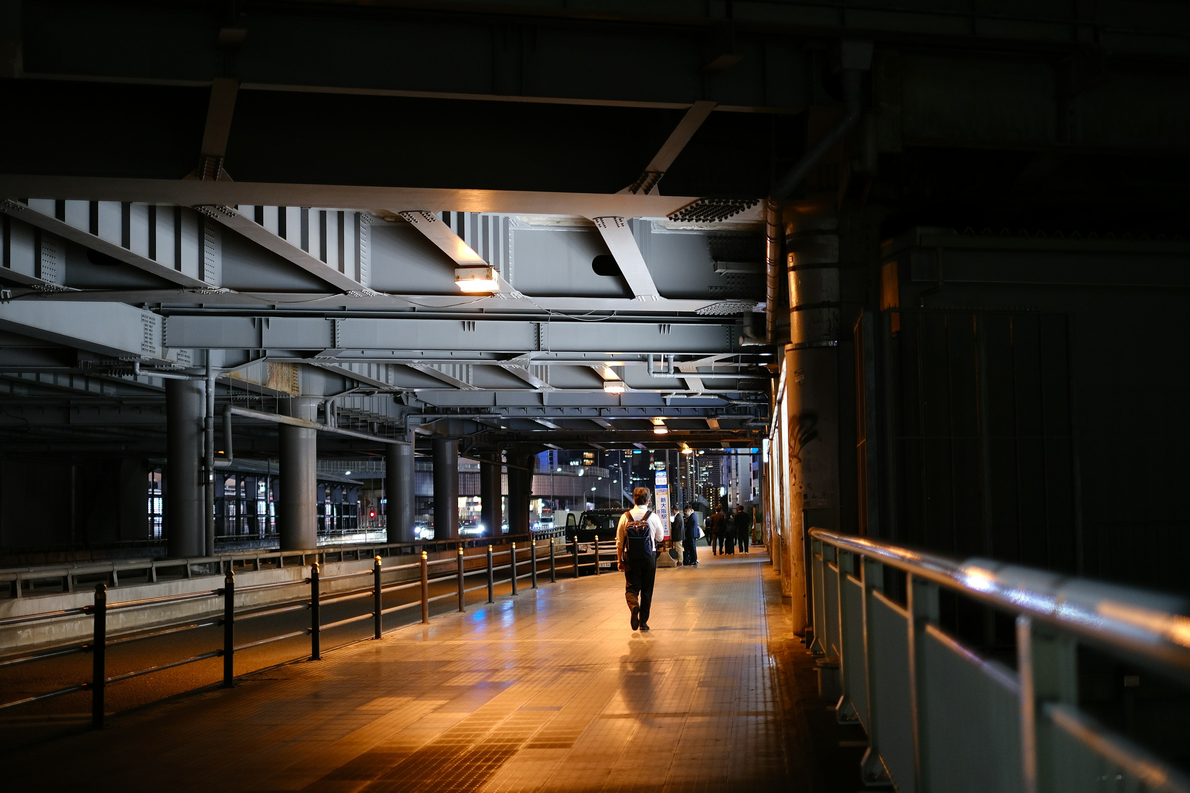 Una figura che cammina in un corridoio industriale debolmente illuminato con travi metalliche