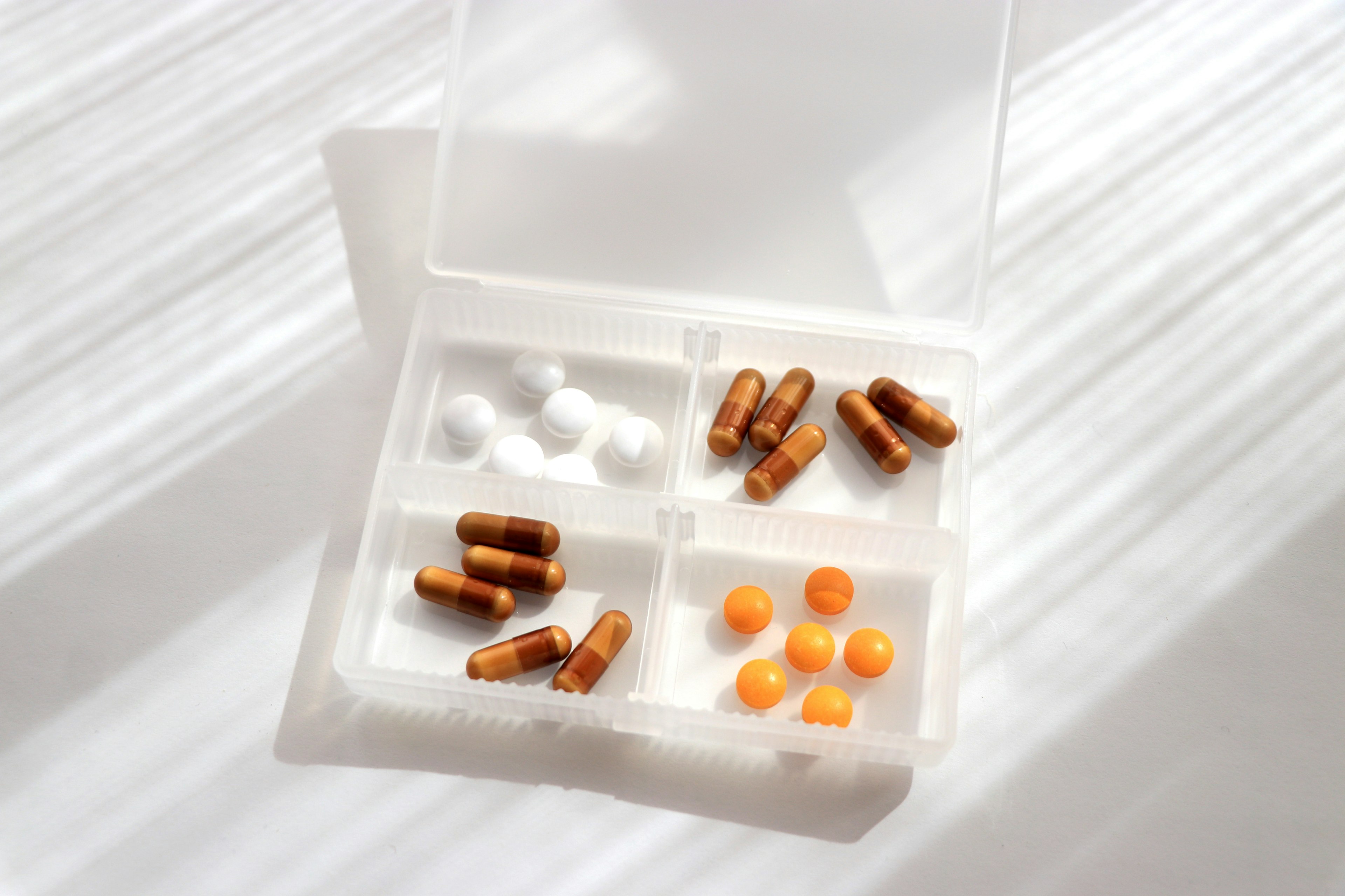 Ein weißer Tablettenorganisator mit braunen Kapseln und orangefarbigen Tabletten, die darin angeordnet sind