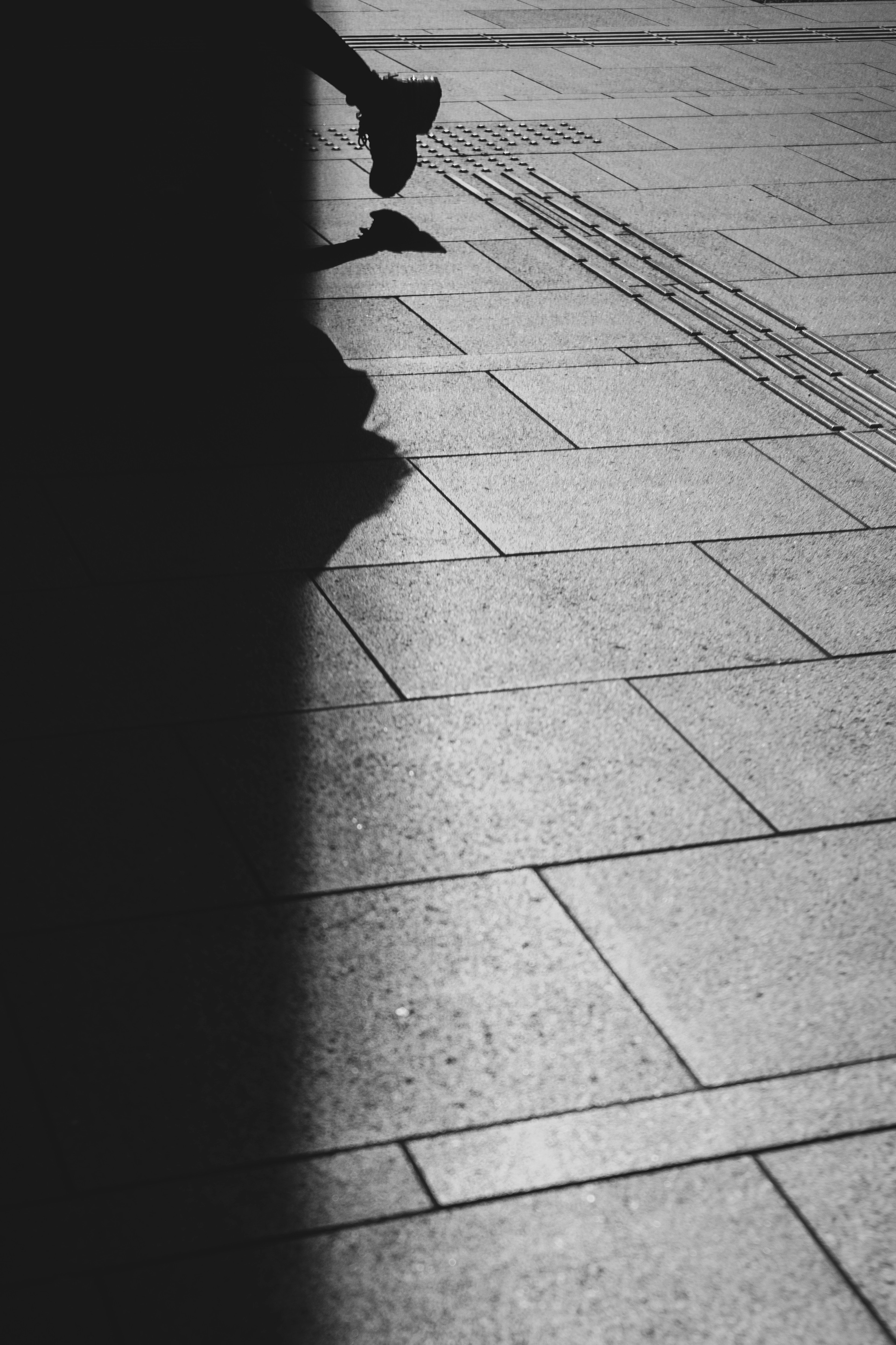 Image monochrome à fort contraste montrant des pieds et un sol carrelé avec des ombres