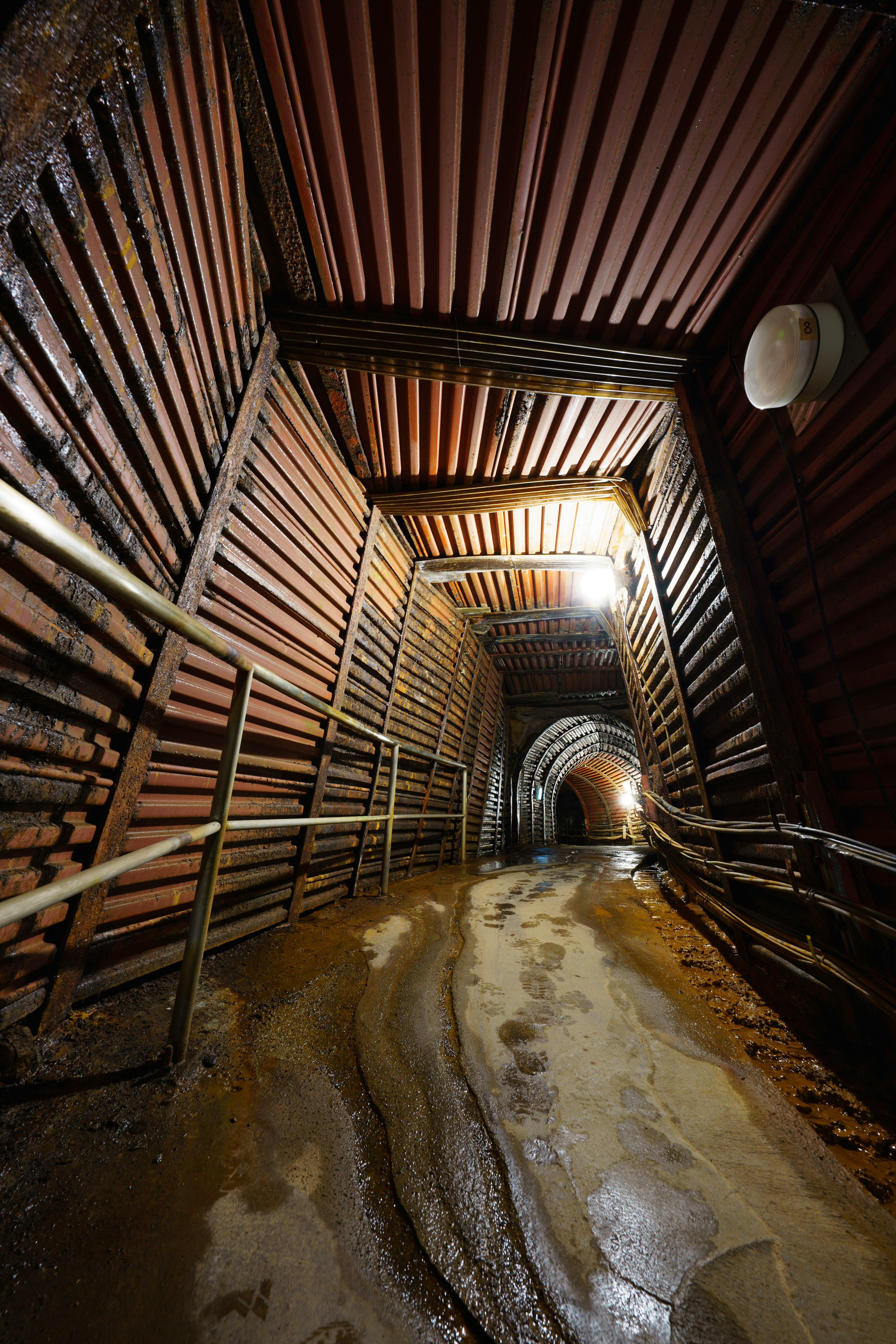 Interior de un largo túnel subterráneo con suelo mojado y barandillas de metal