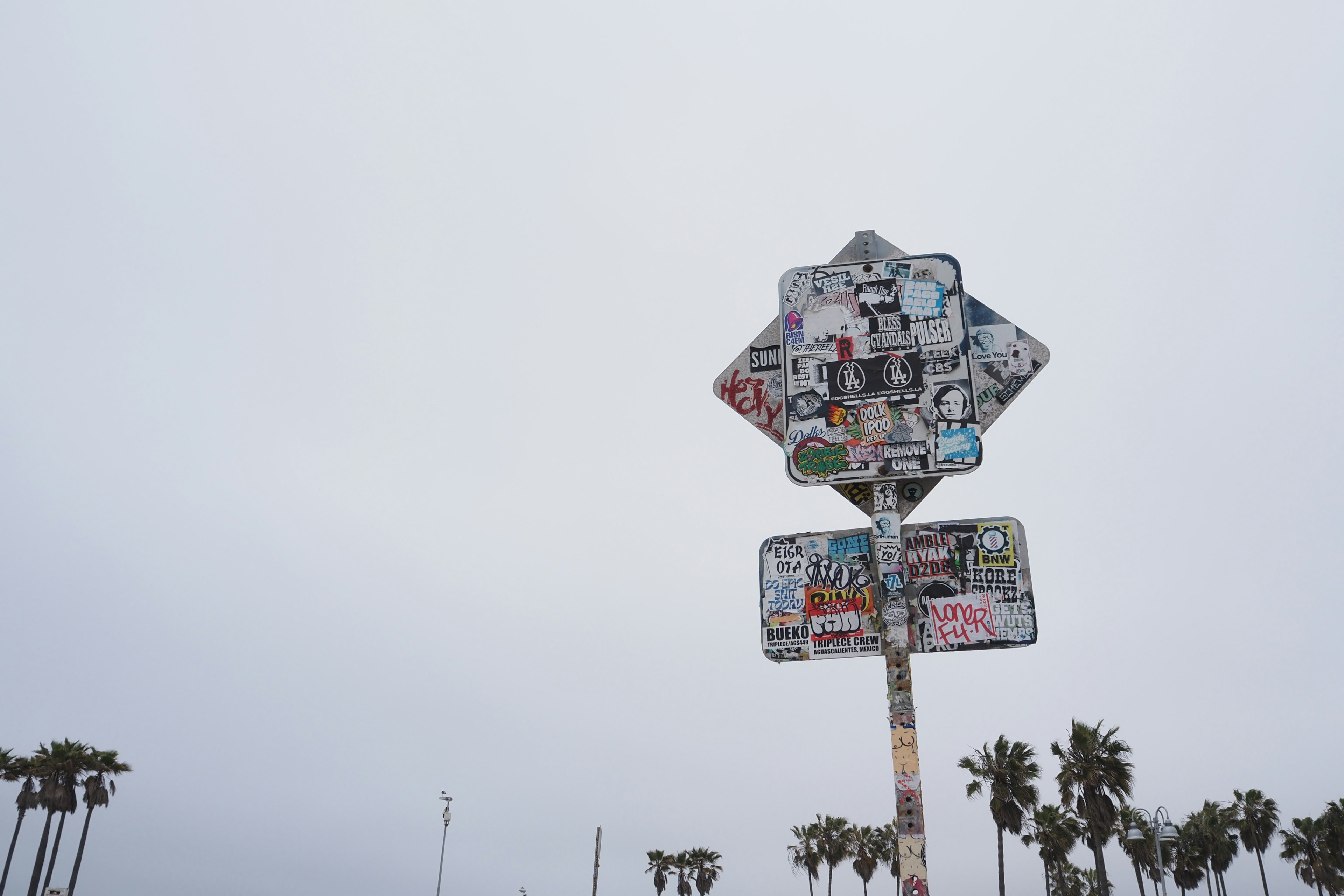 A weathered sign covered in various stickers under a cloudy sky