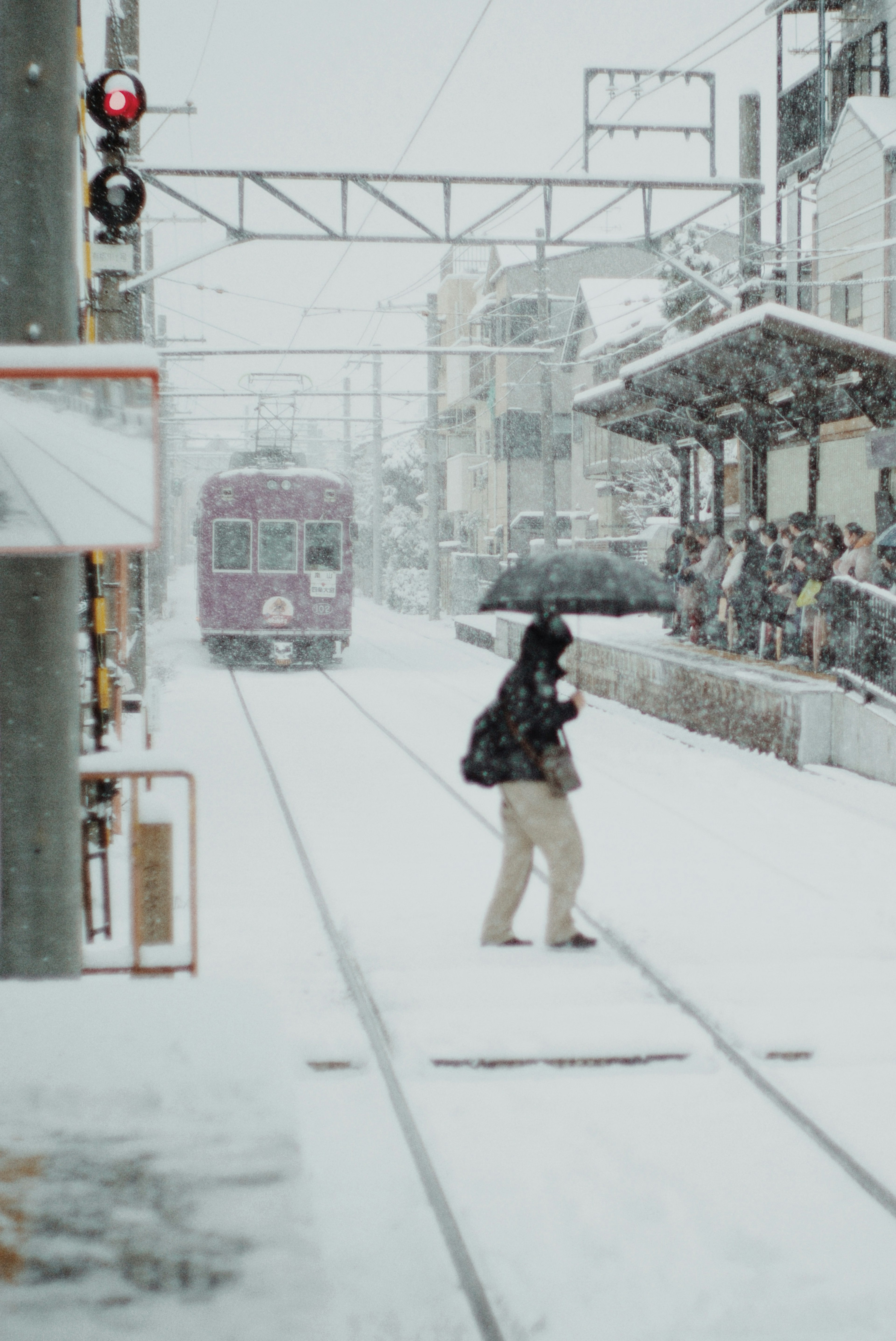 Una persona con un paraguas cruzando vías de tren nevadas en una estación