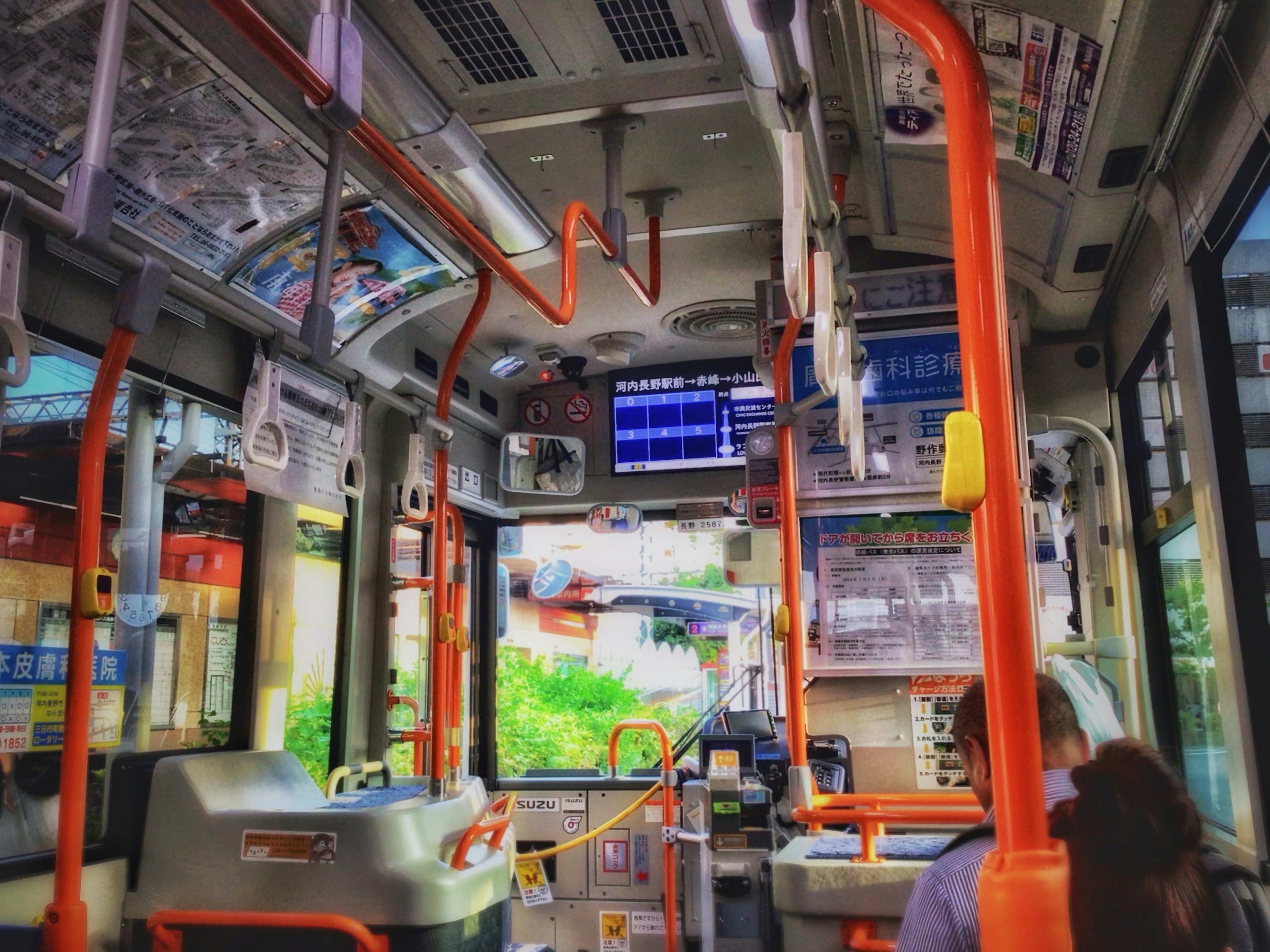 Interno di un autobus con corrimano arancioni e un monitor digitale