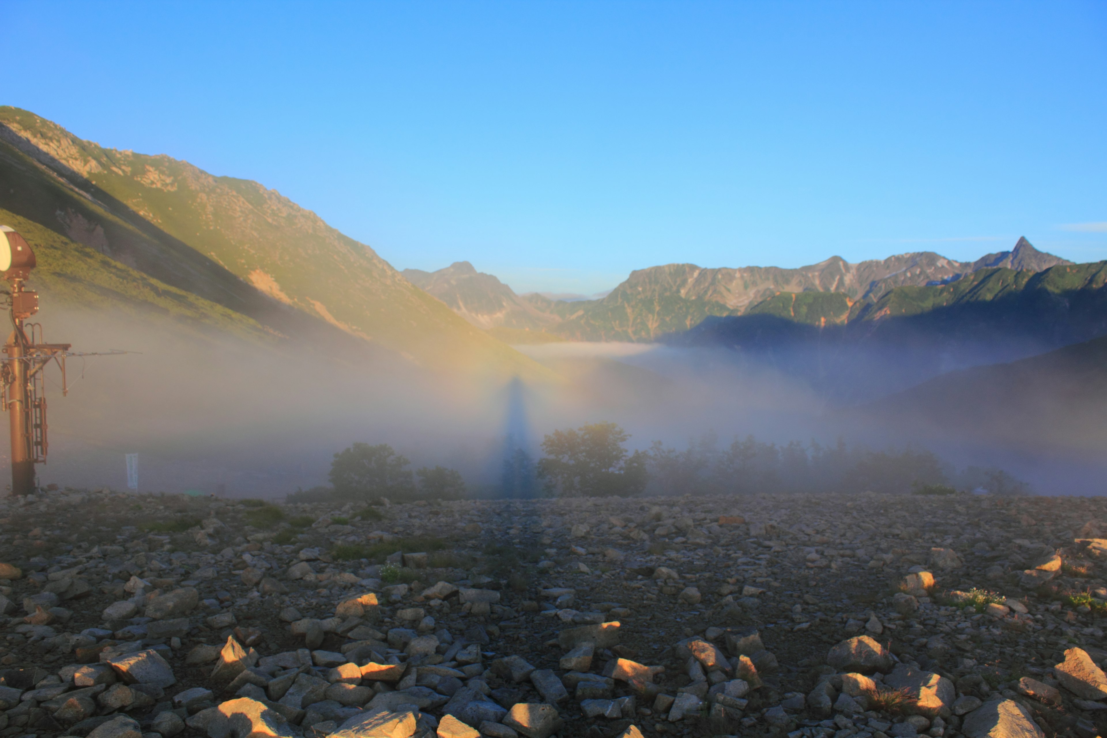 Paysage montagneux enveloppé de brouillard avec un ciel bleu clair et un premier plan rocheux