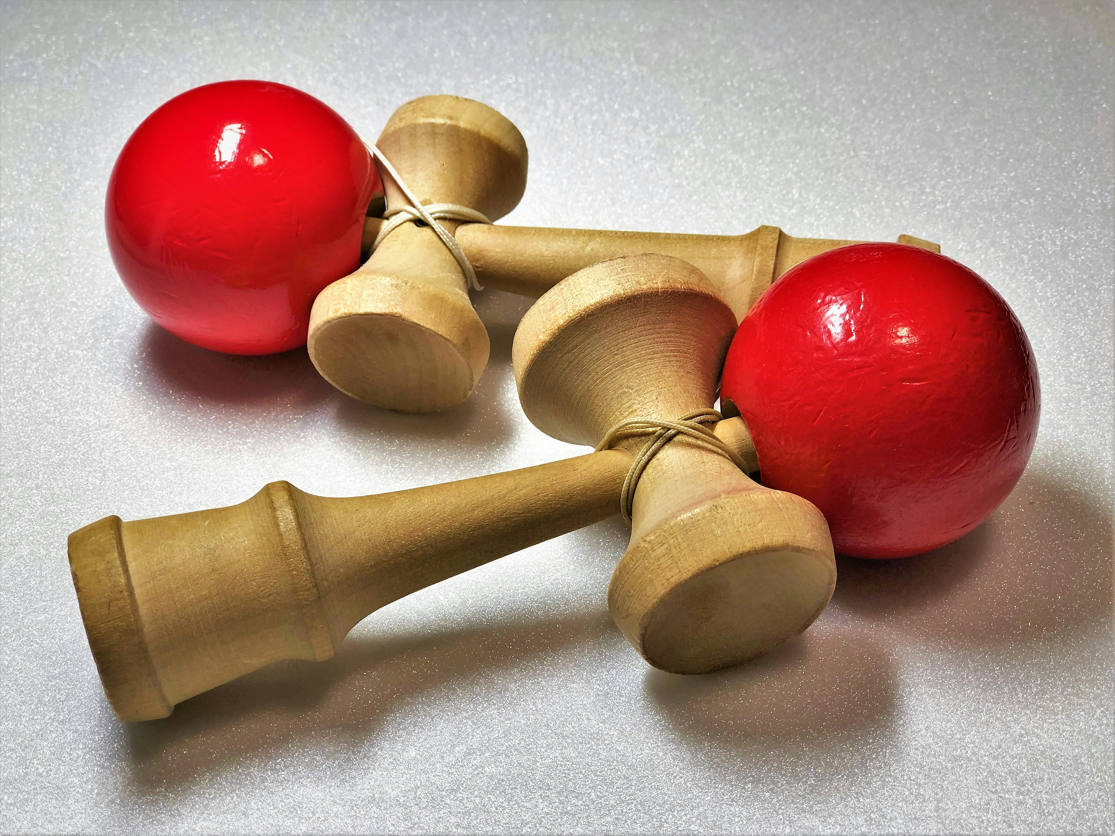 Two kendama toys with red balls and wooden handles on a light surface