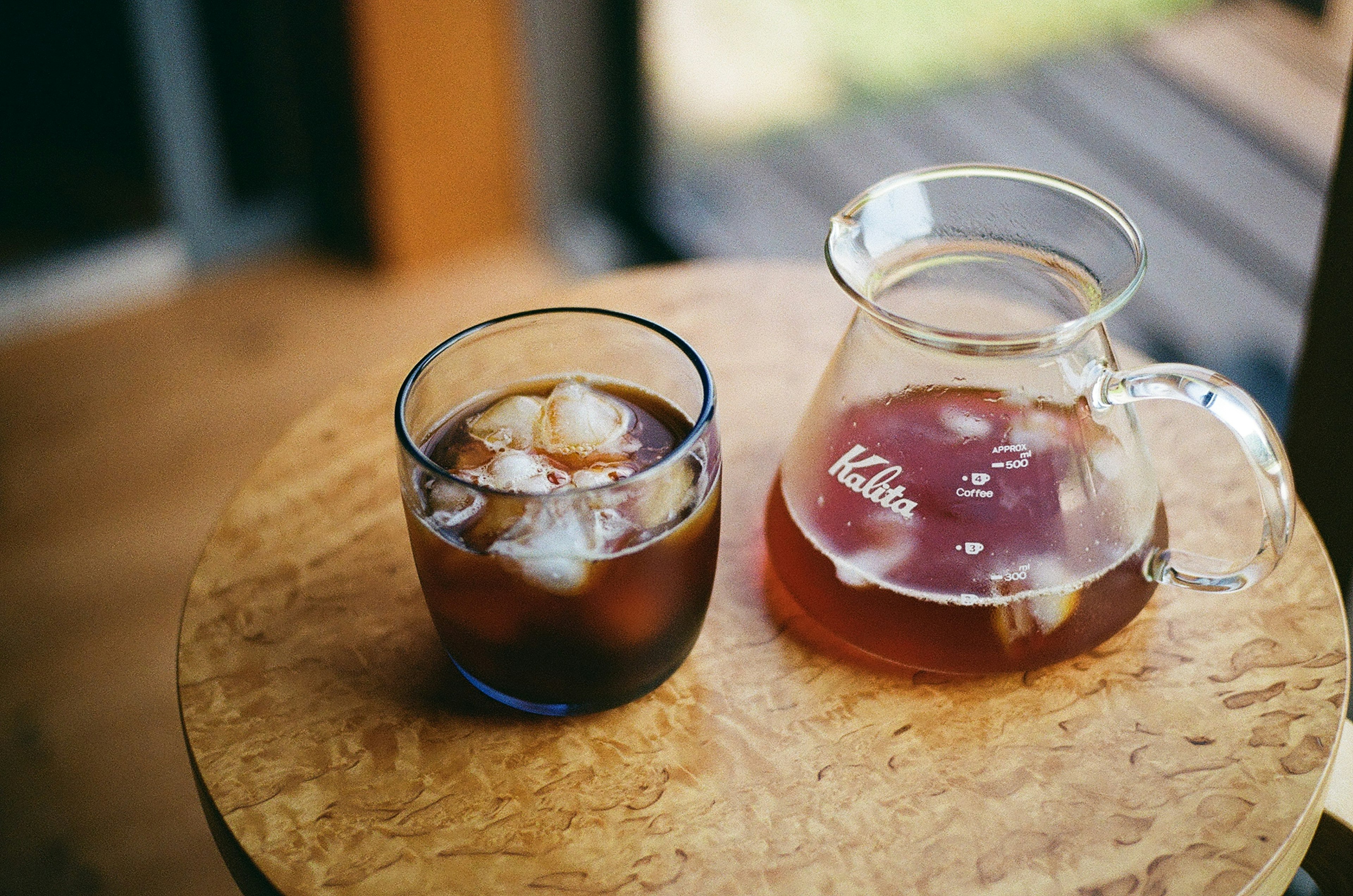 Un vaso de café helado y una jarra sobre una mesa de madera