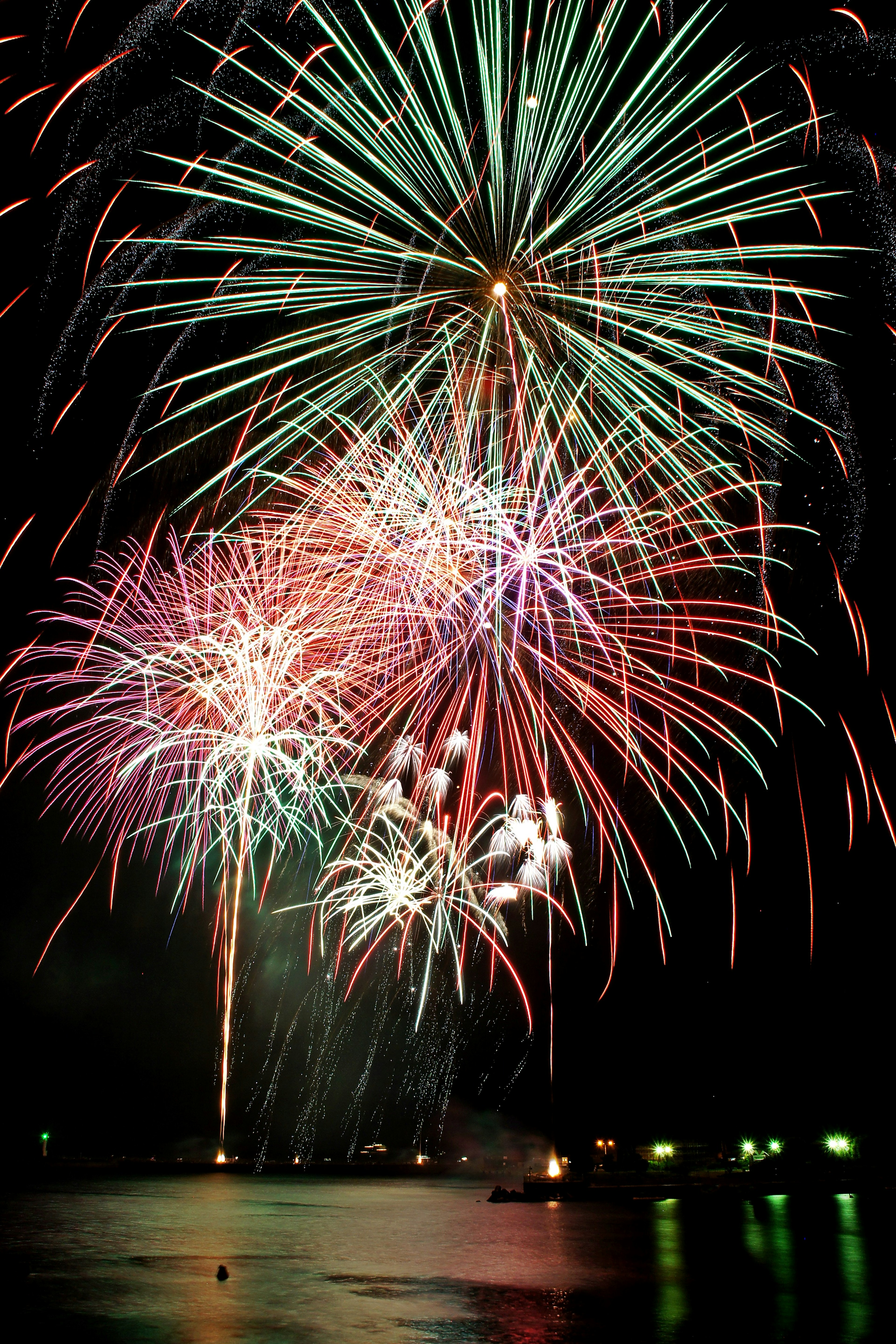 Fuochi d'artificio colorati che esplodono nel cielo notturno riflettendosi sull'acqua