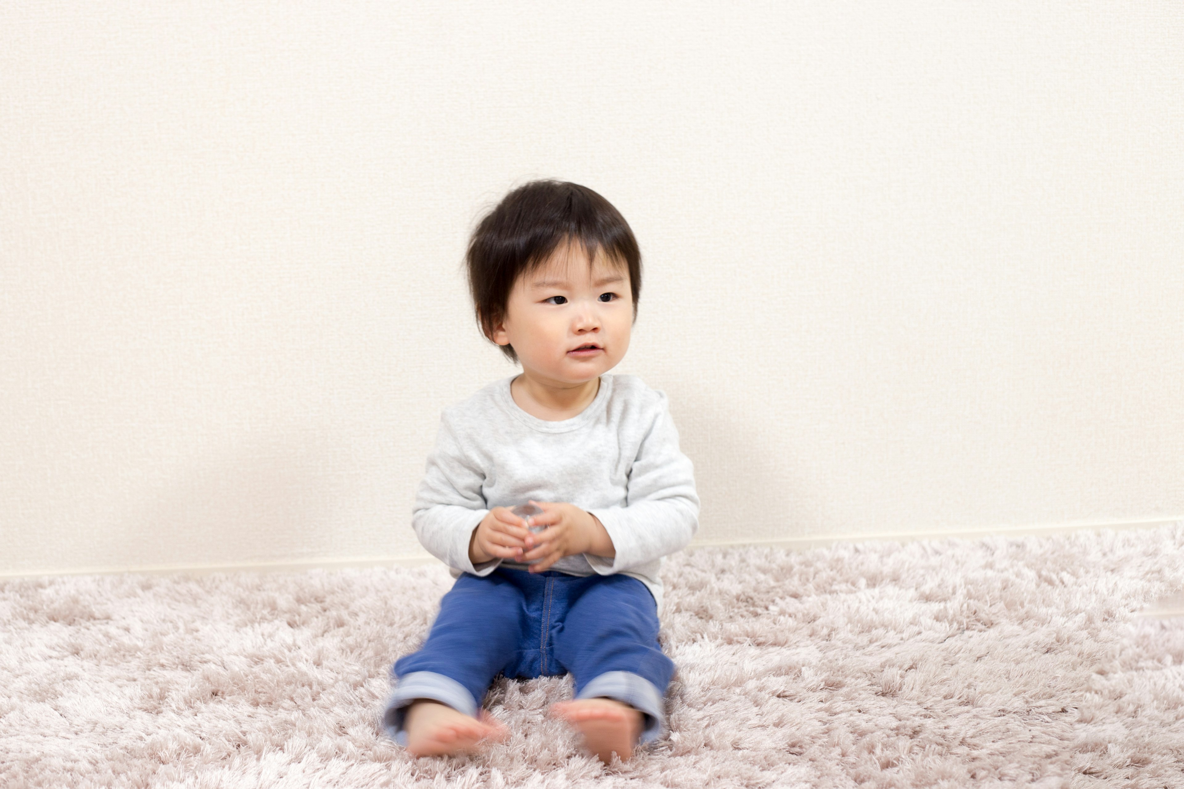 Seorang anak kecil duduk di atas karpet lembut di depan dinding polos