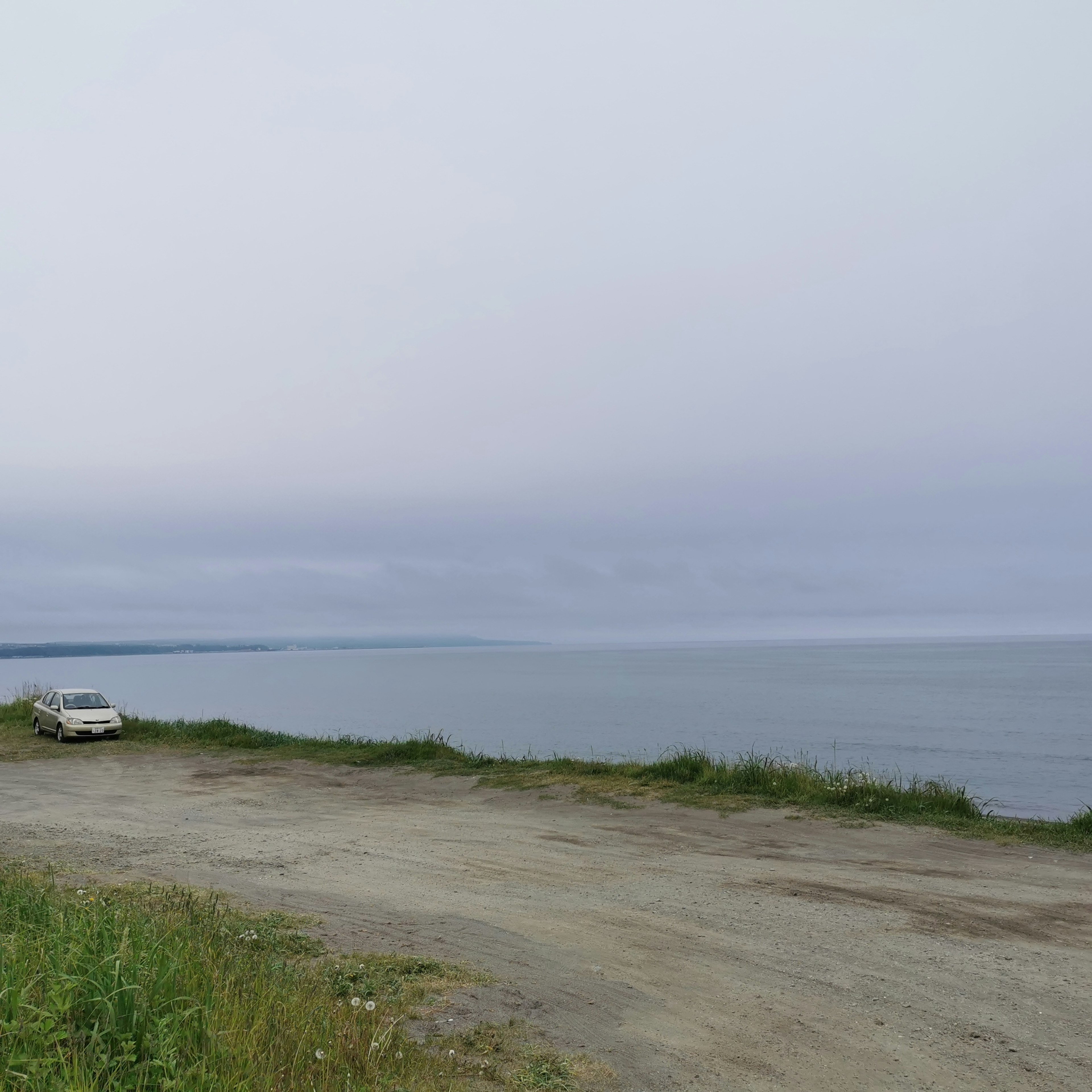 A car parked near a calm sea under a cloudy sky