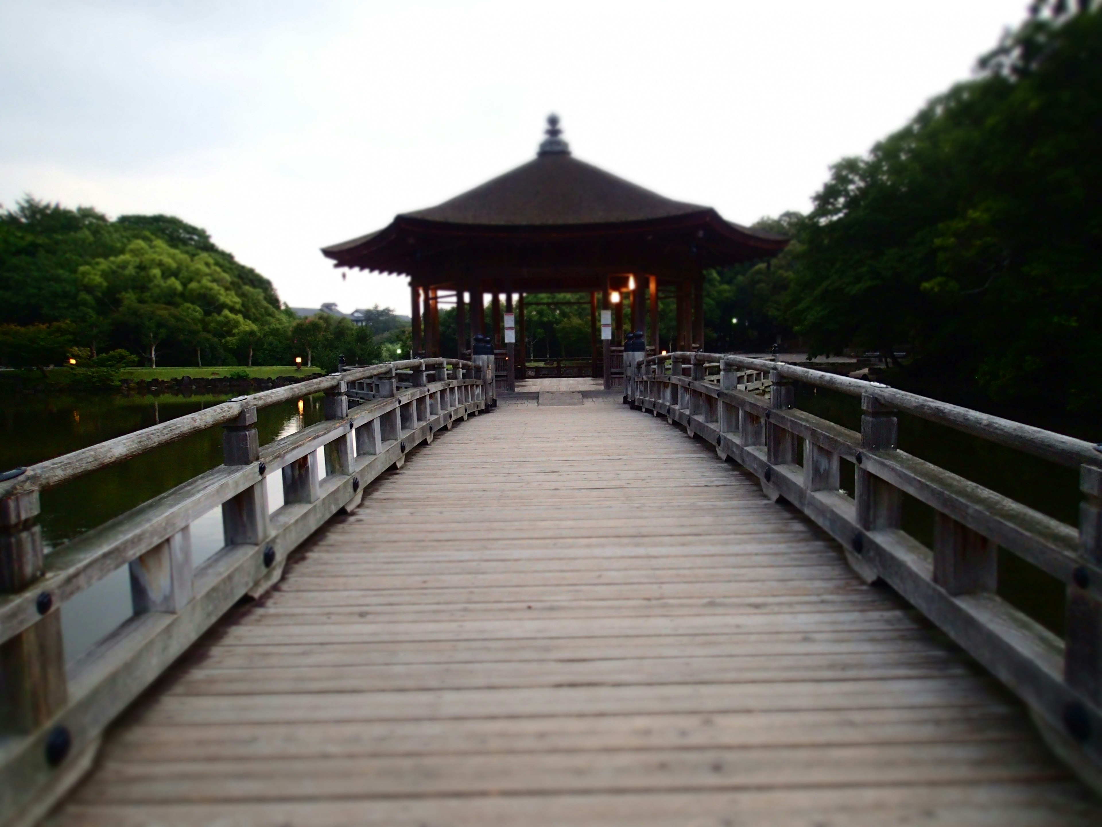 A scenic wooden bridge leading to a small pavilion over a tranquil pond