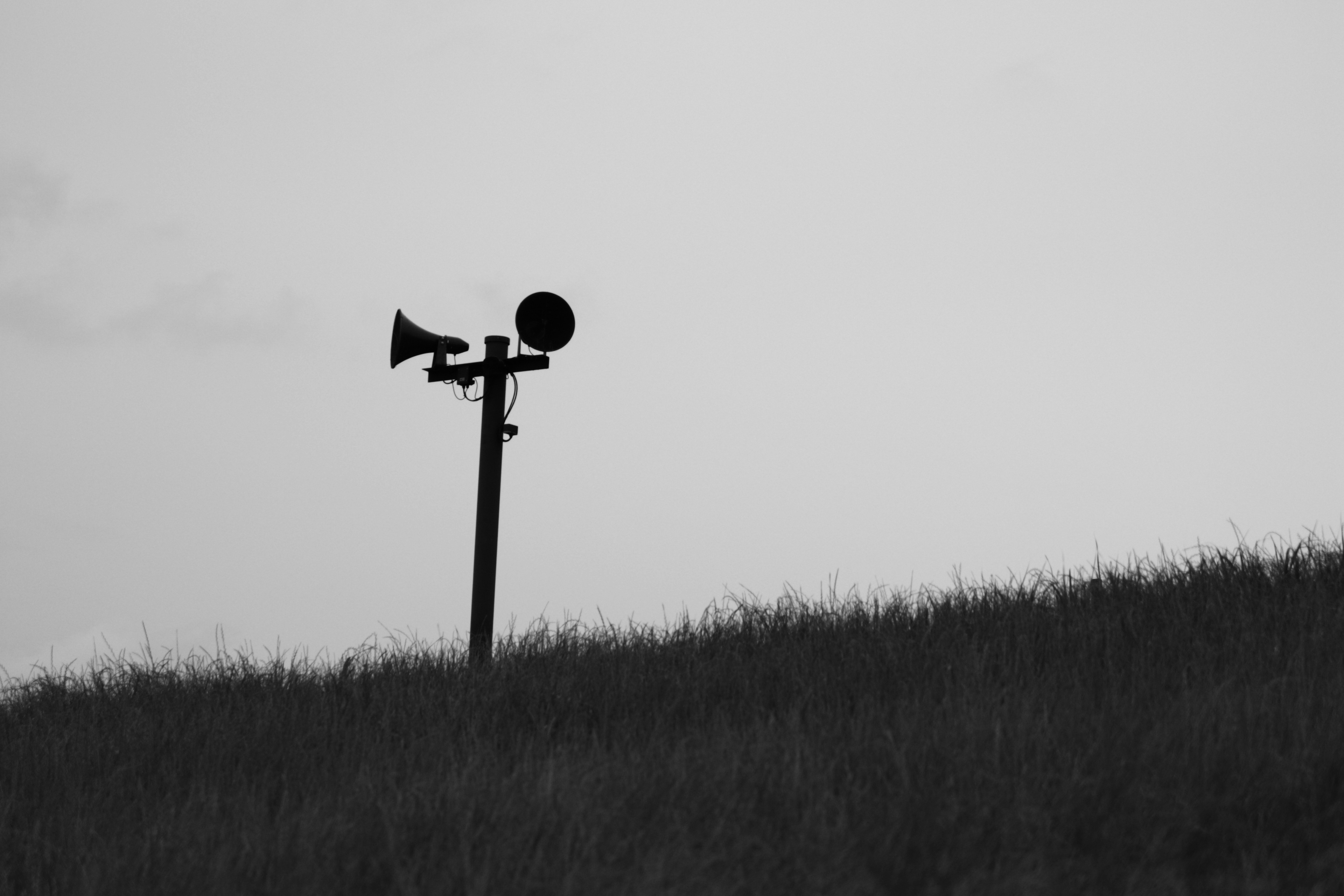 Silhouette of a warning siren and speaker against a black and white landscape