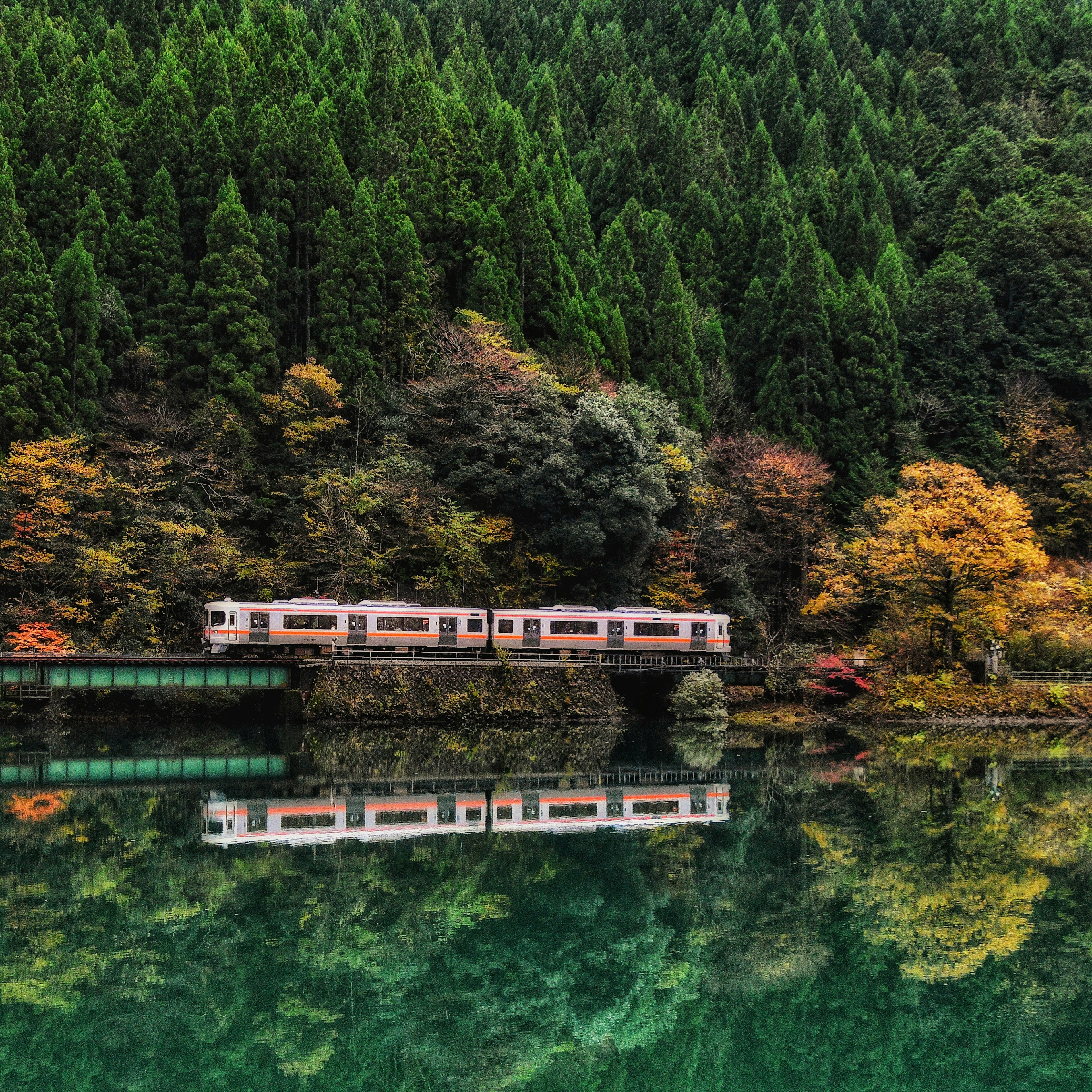 Train reflecting on a serene green lake surrounded by colorful autumn trees