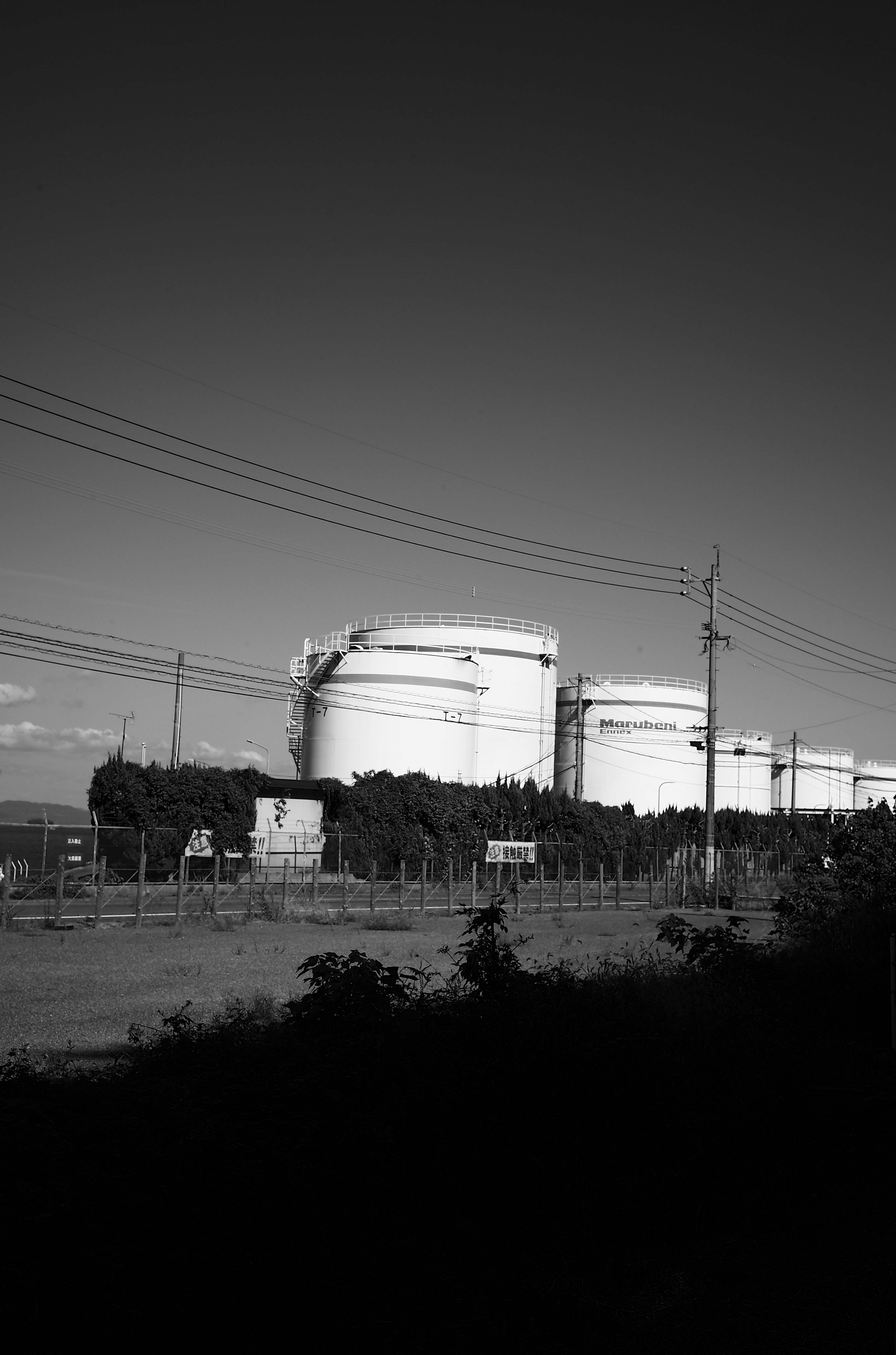 白黒の油槽と電柱が並ぶ風景