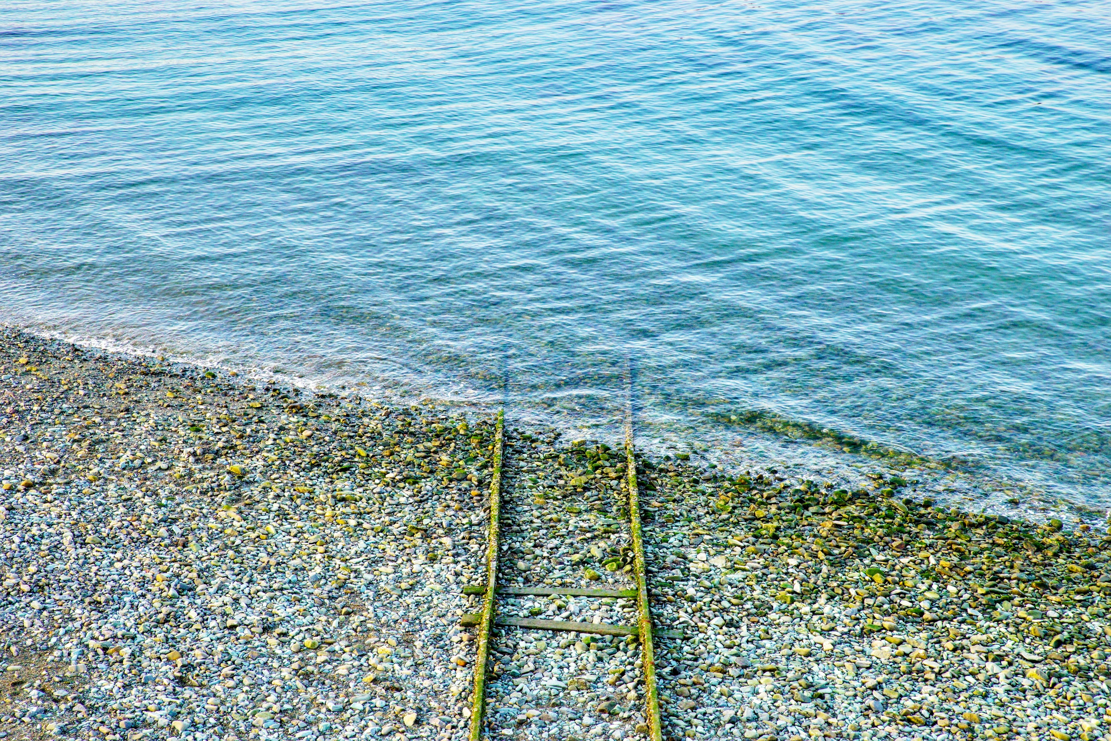 Holzstufen, die zu ruhigem Wasser und einem Kiesstrand führen