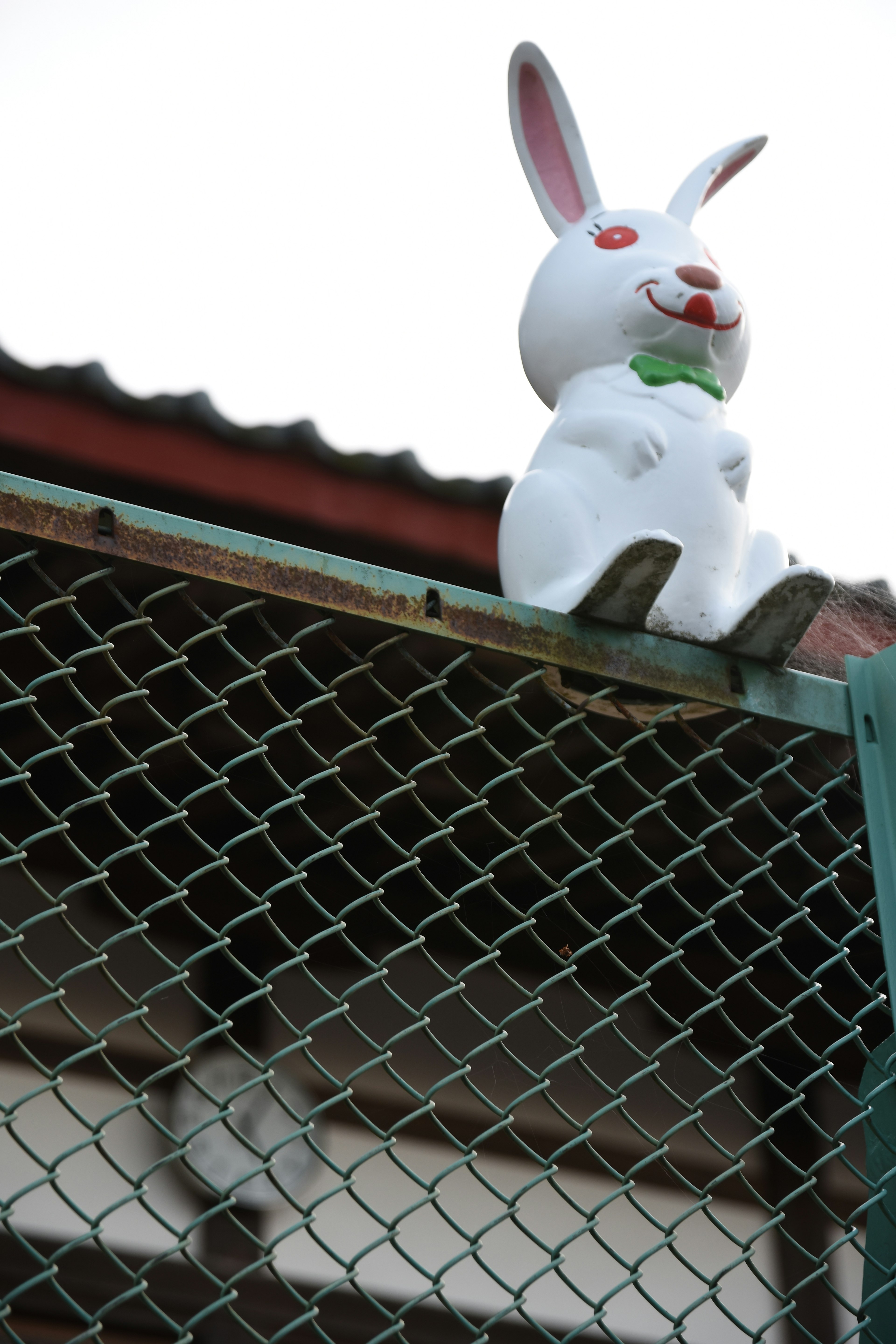 Figura de conejo blanco sentada en un techo con ojos rojos y un moño verde