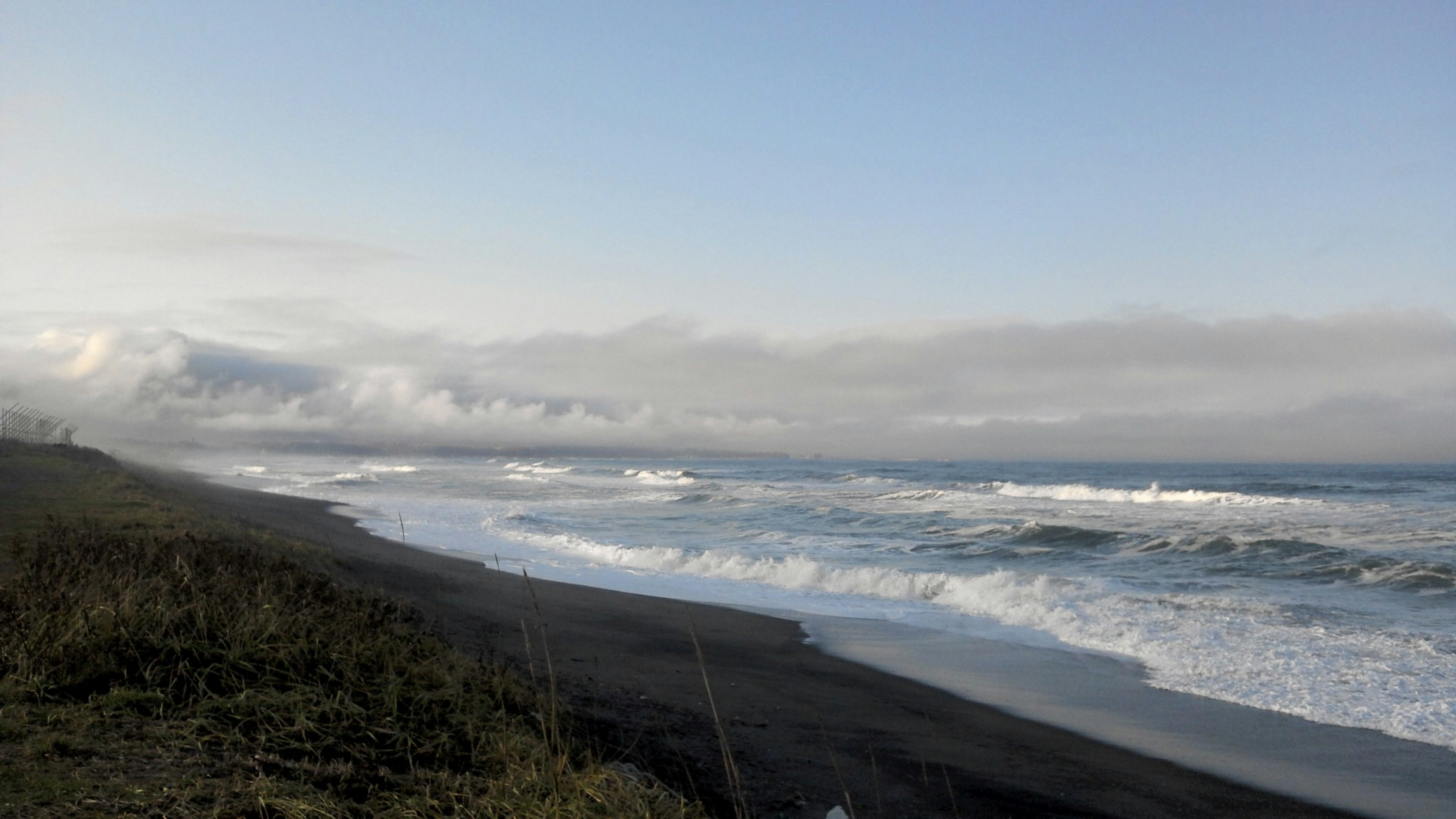 Coastal landscape with blue sky and ocean waves black sandy beach and grass