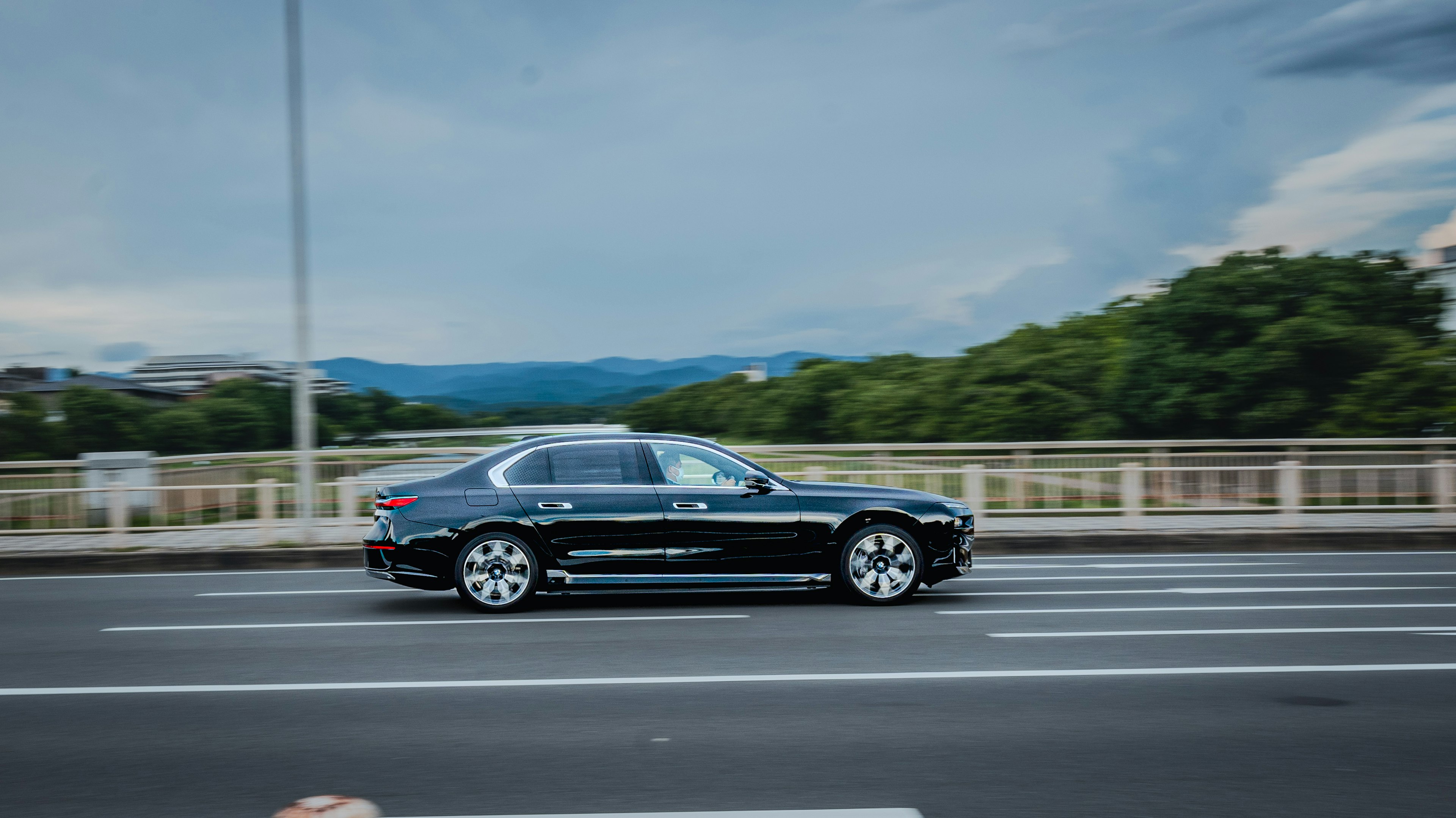 A black luxury car driving on a bridge with a scenic background