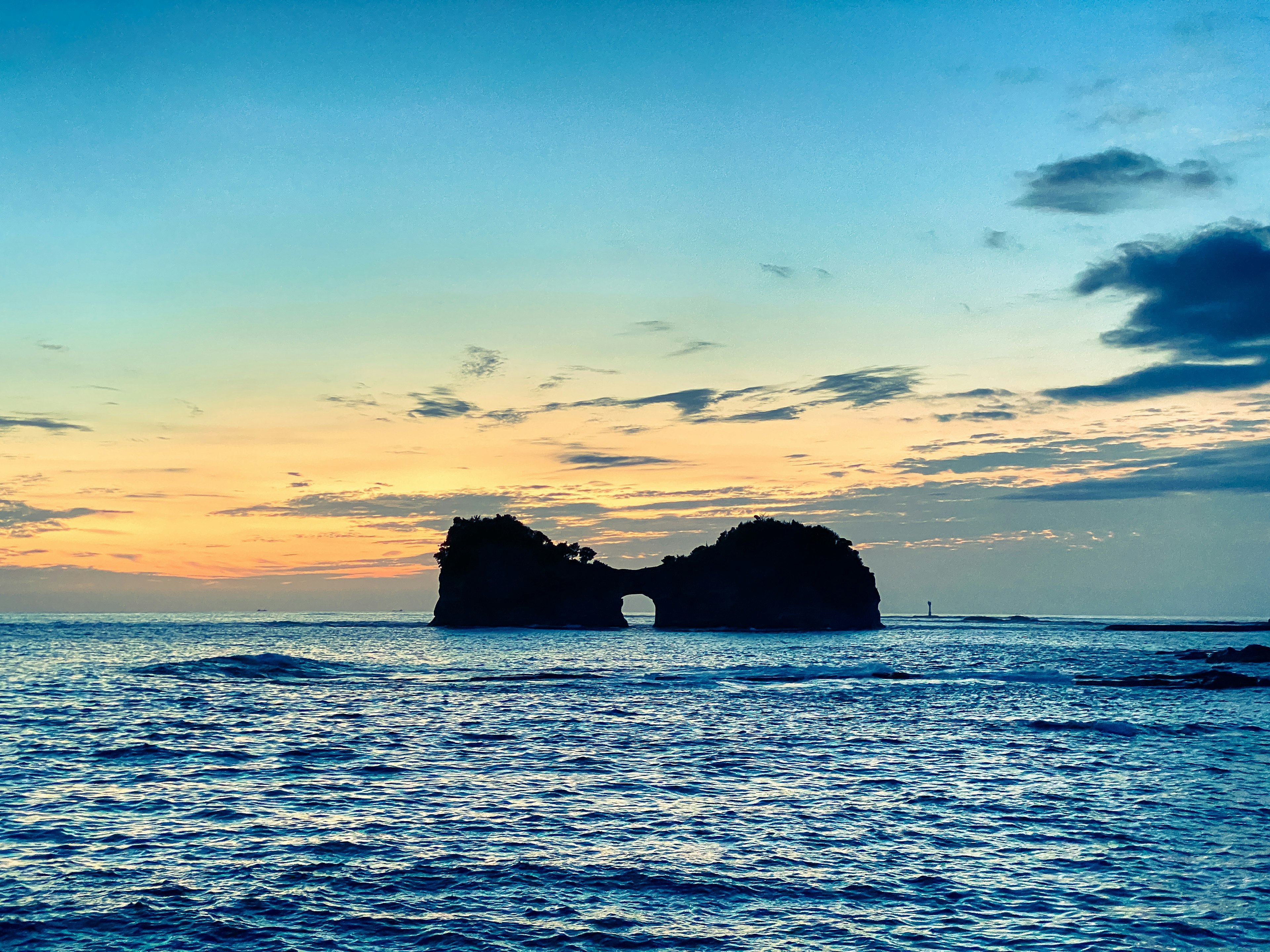 A rock arch in the ocean illuminated by sunset