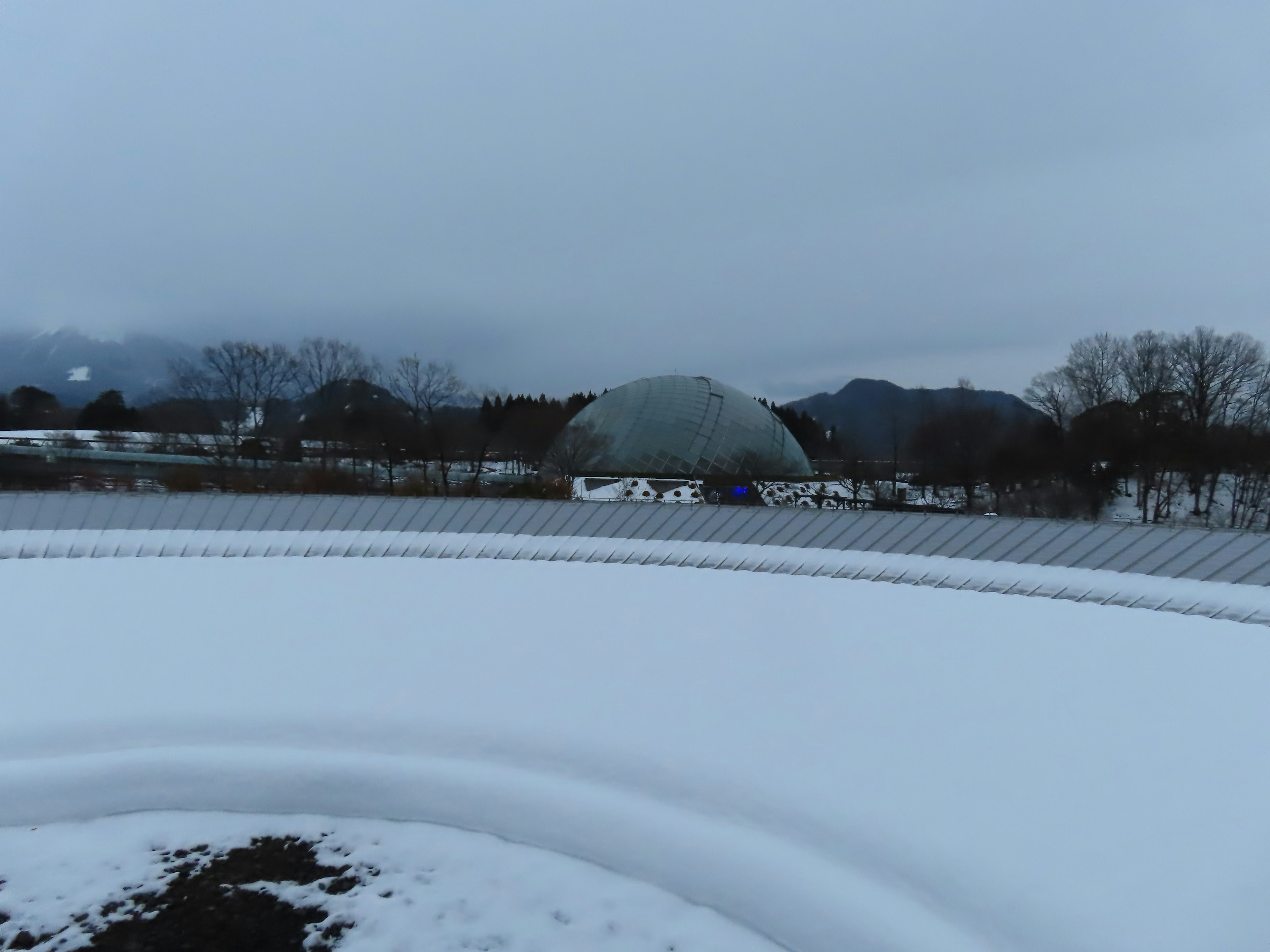 Paisaje cubierto de nieve con un edificio en forma de cúpula y montañas al fondo