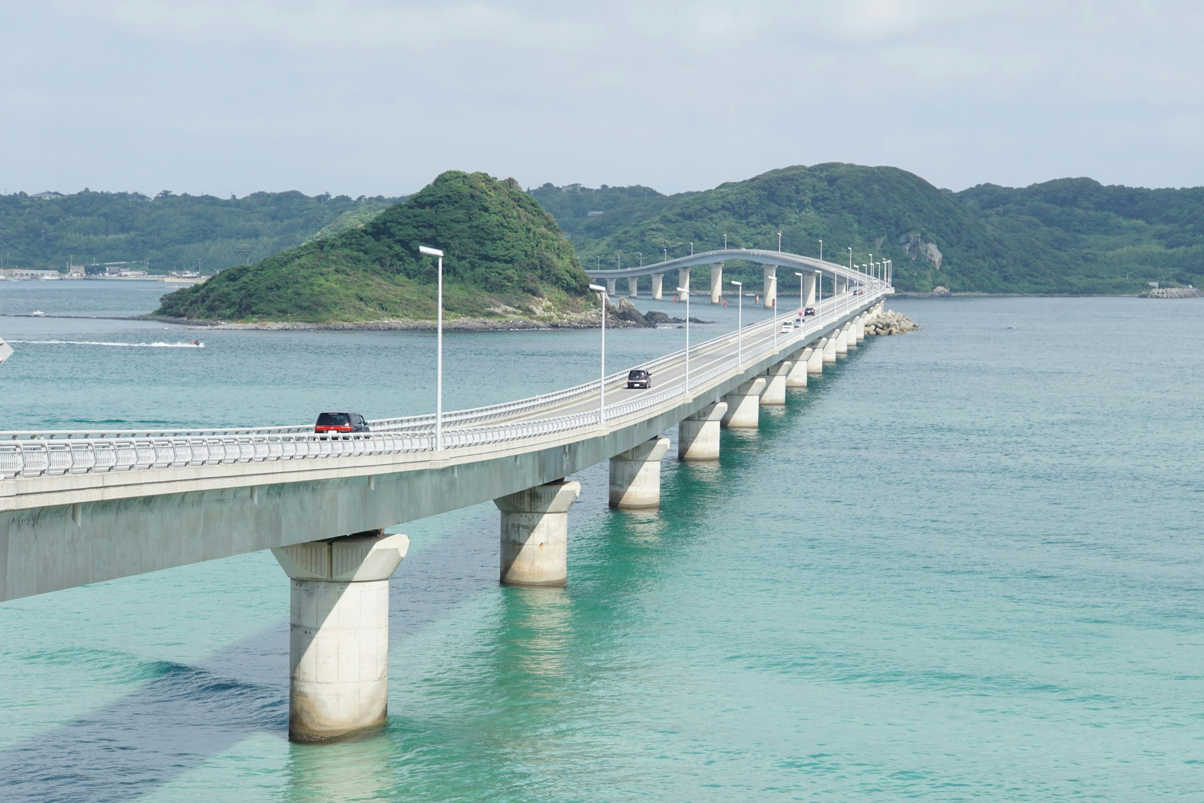 A scenic bridge spanning turquoise waters with a green island in the background