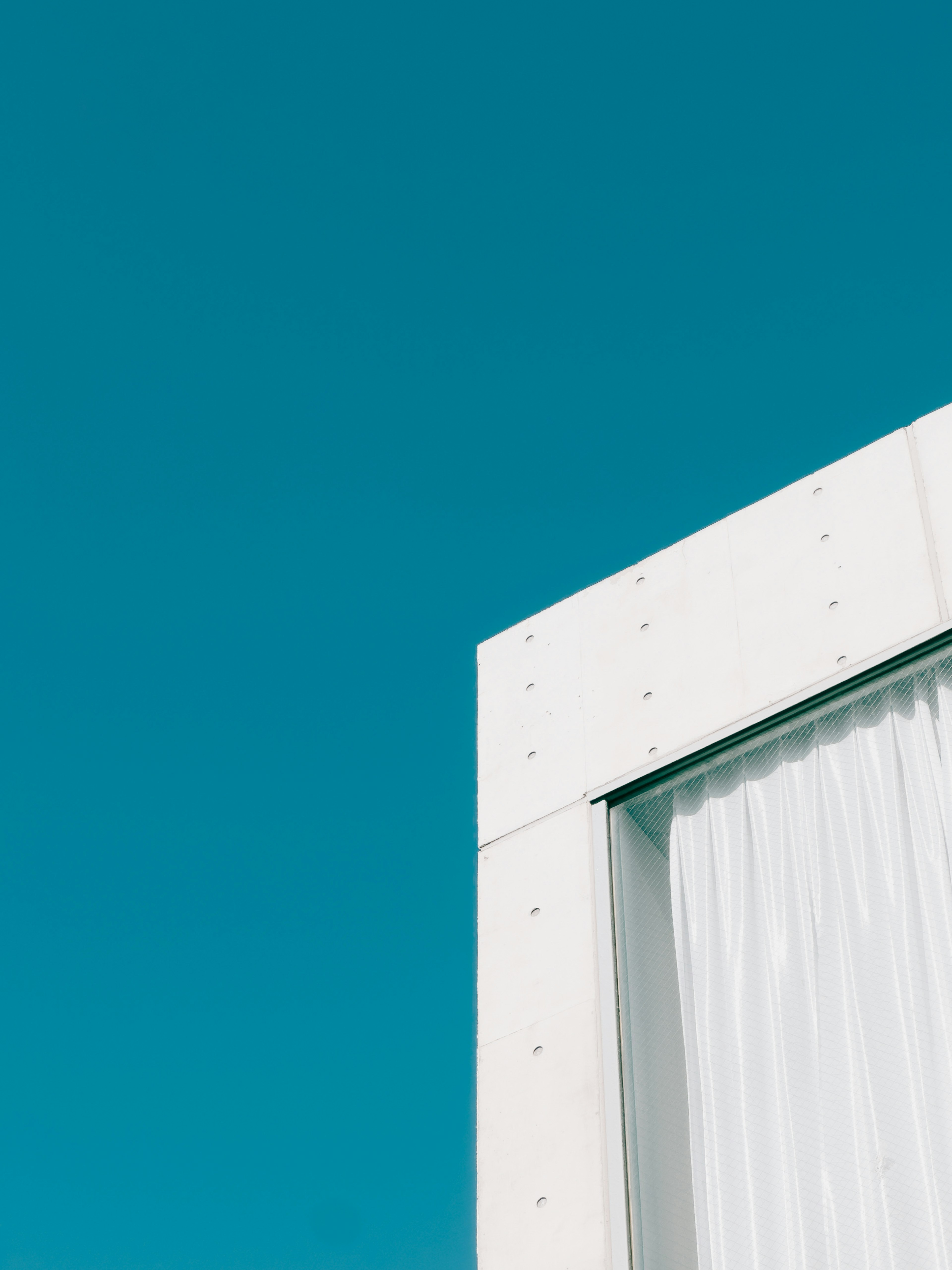 Modernes architektonisches Detail mit weißen Vorhängen vor einem hellblauen Himmel