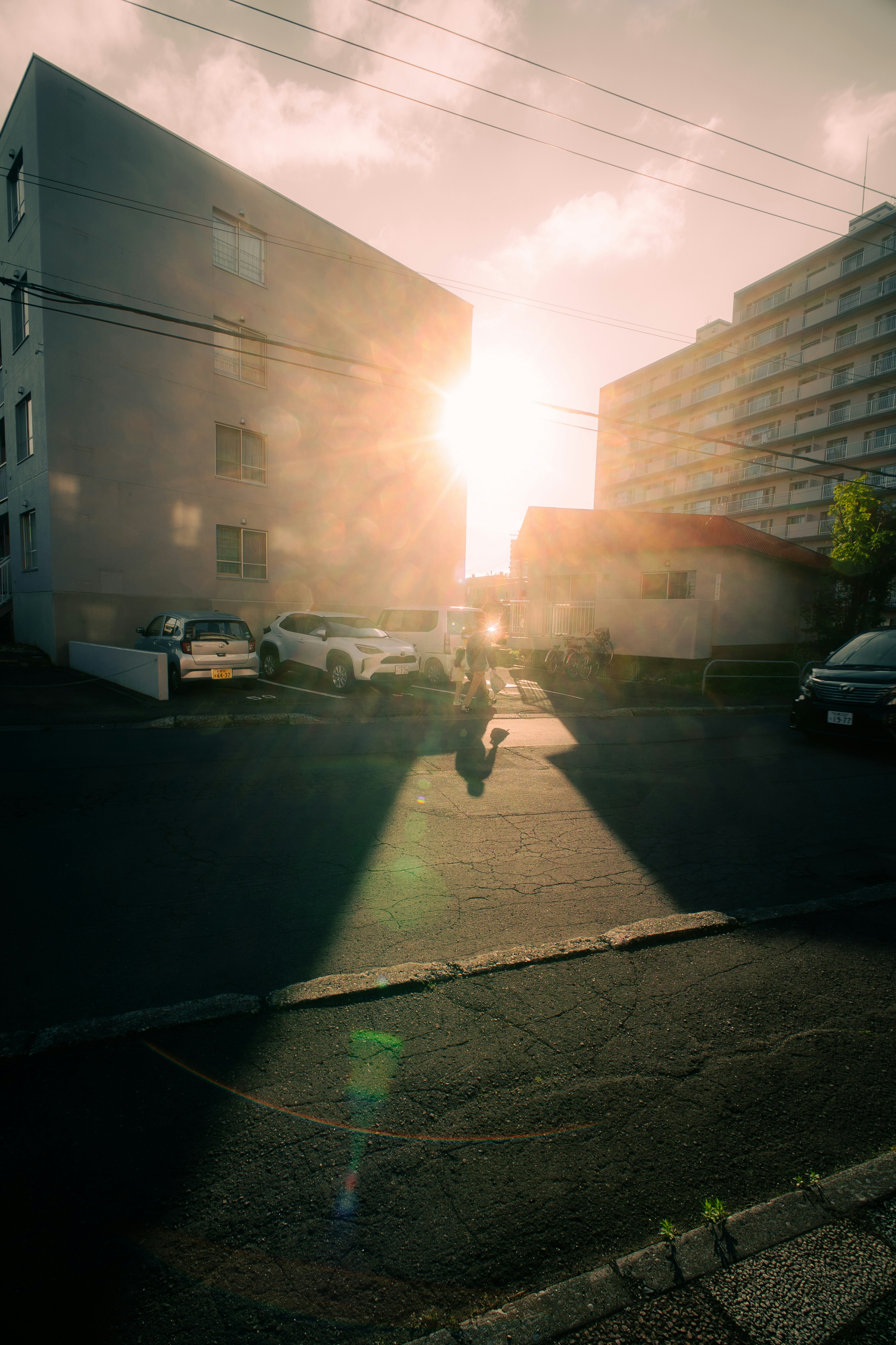 Beautiful view of sunset shining between buildings with parked cars and silhouettes