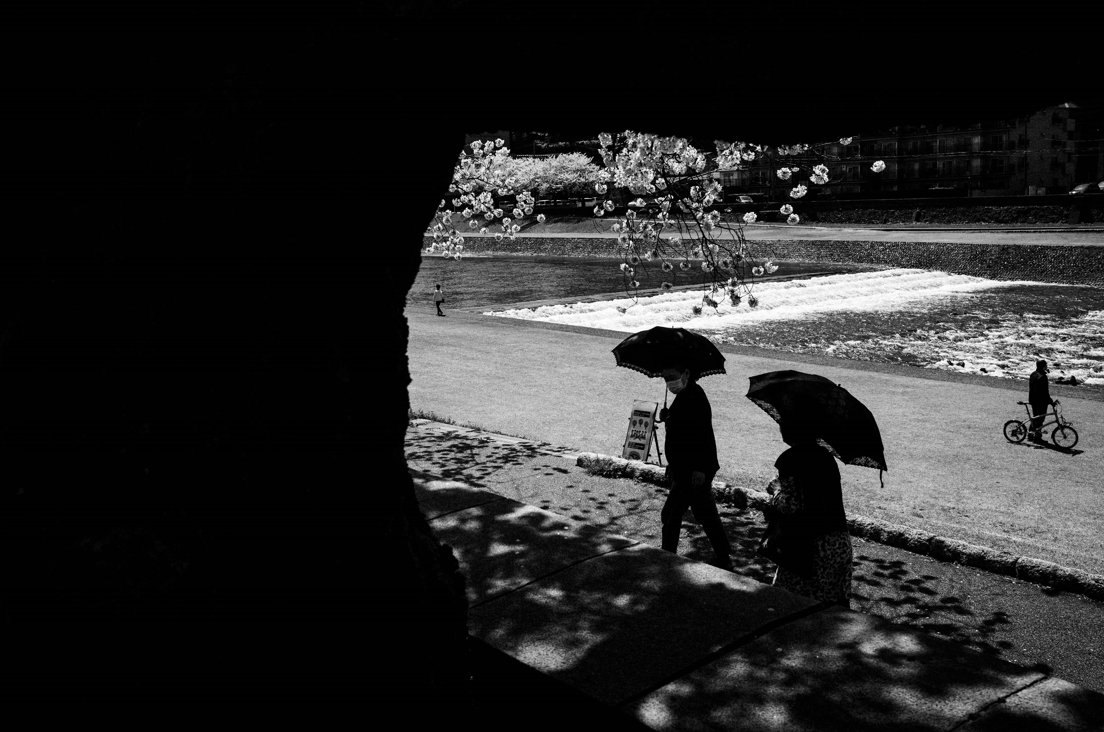 Dos figuras caminando con paraguas en una escena sombría