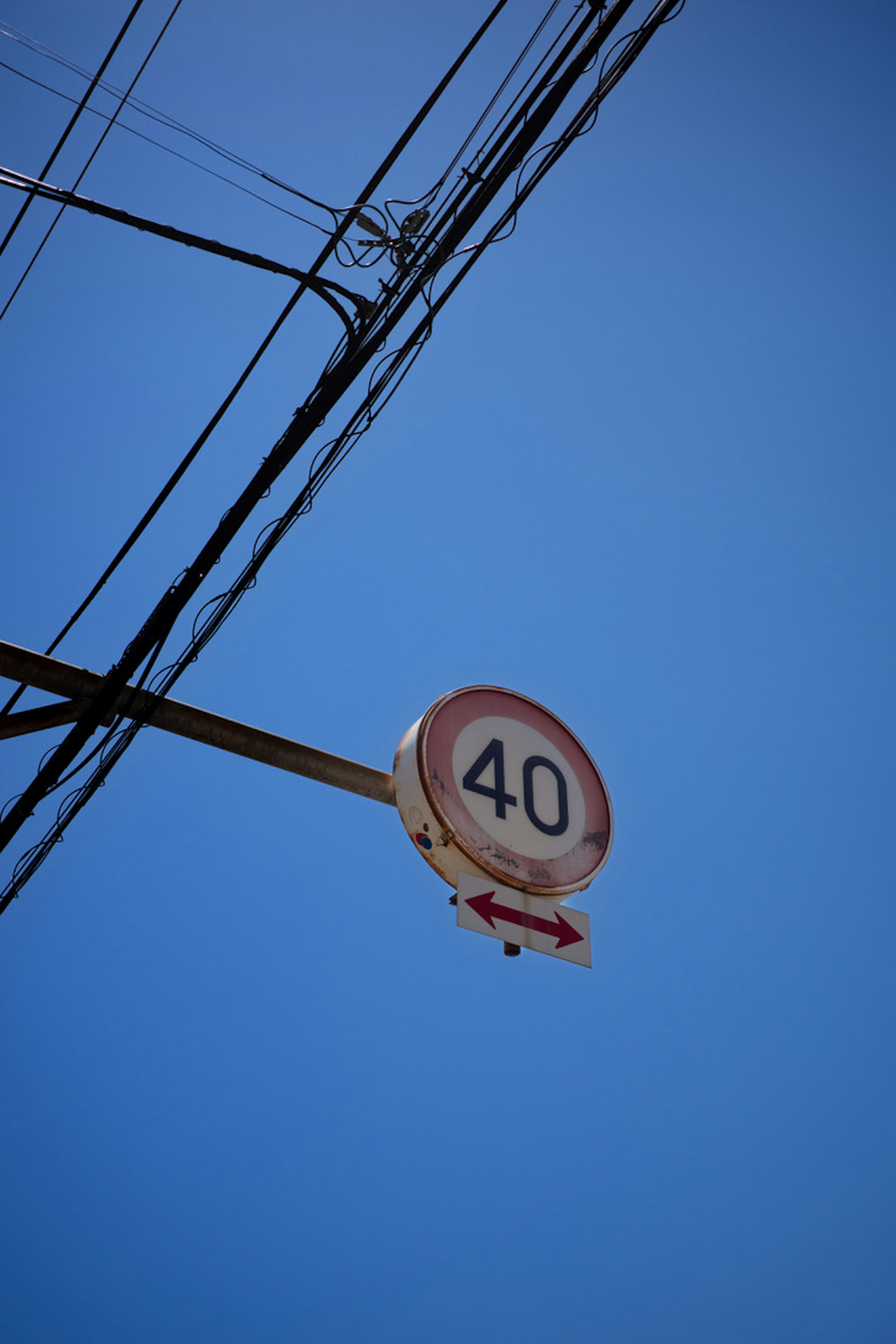 Cartello di limite di velocità che indica 40 km/h sotto un cielo blu chiaro con cavi elettrici