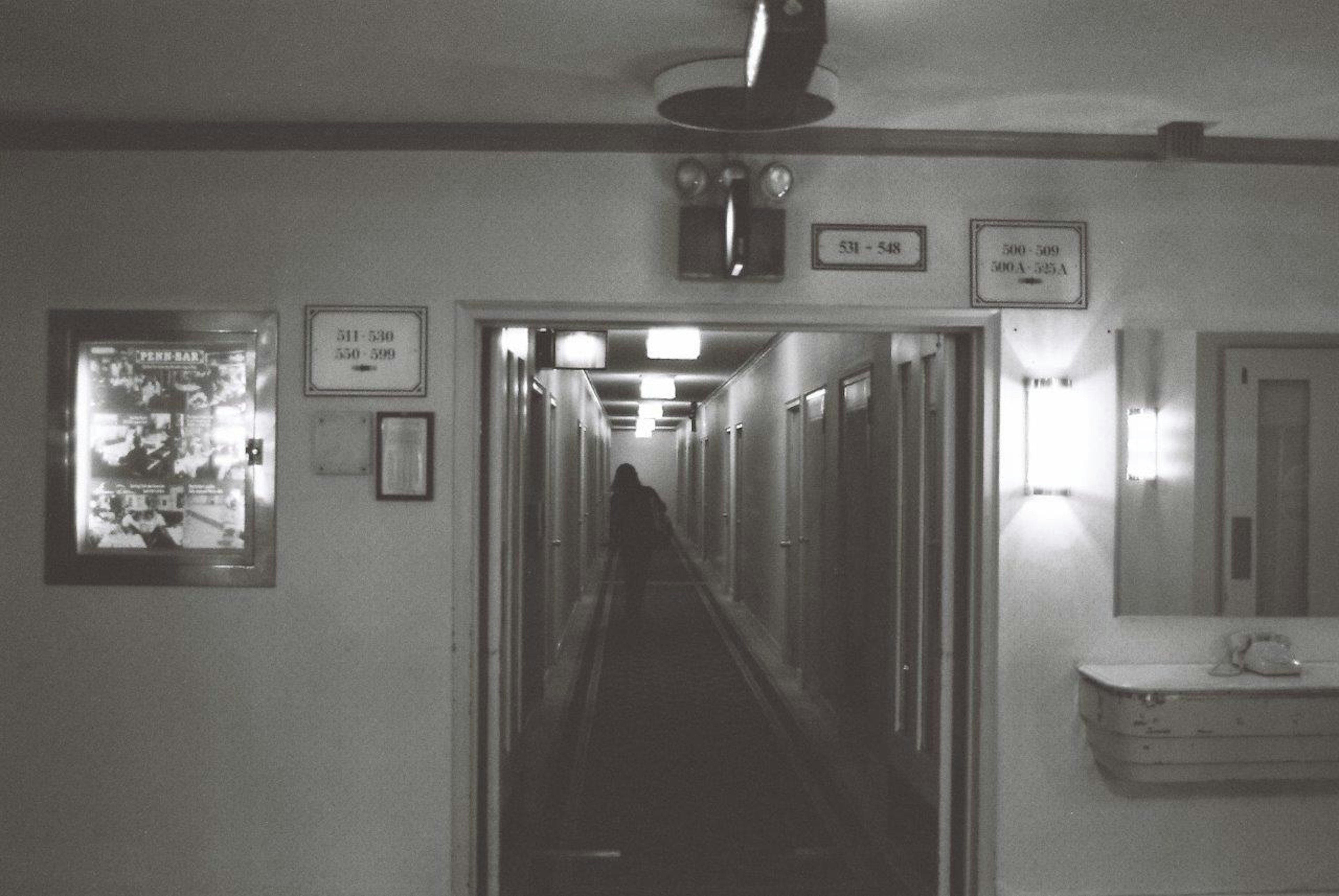 Black and white image of a corridor lined with lamps and signs