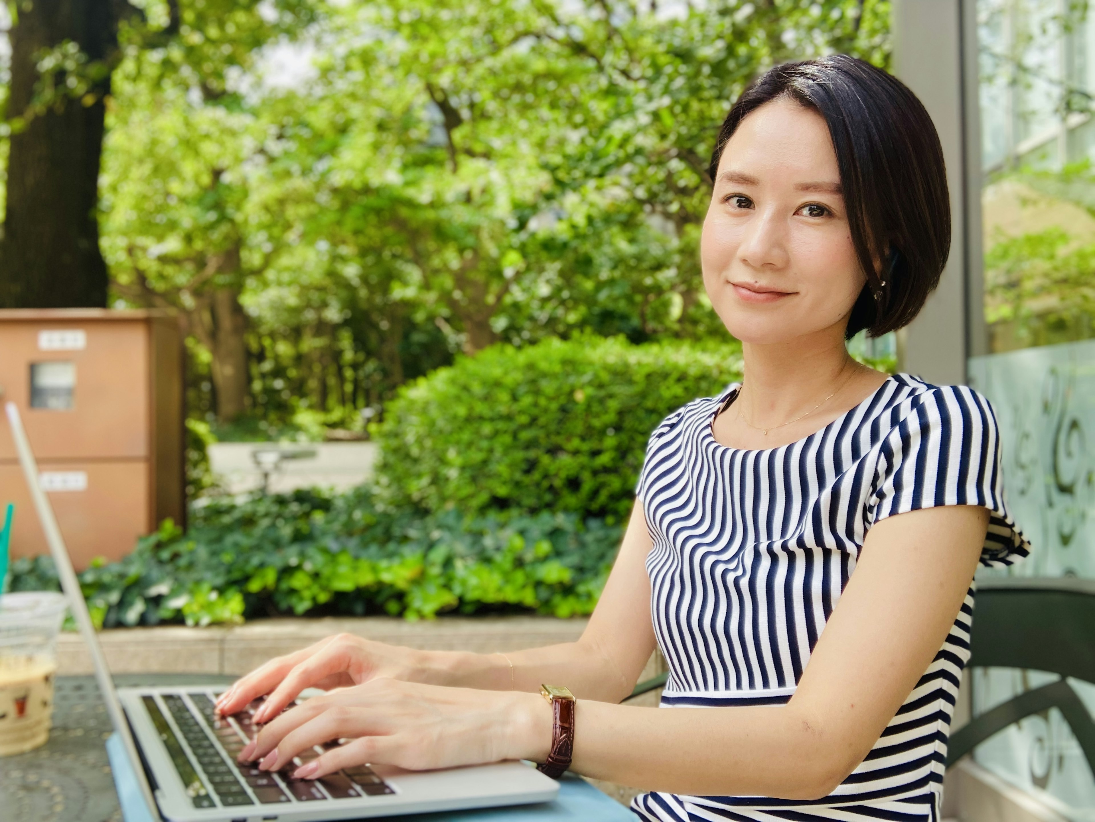 Frau, die in einem Park einen Laptop benutzt Grüner Hintergrund Gestreiftes Hemd