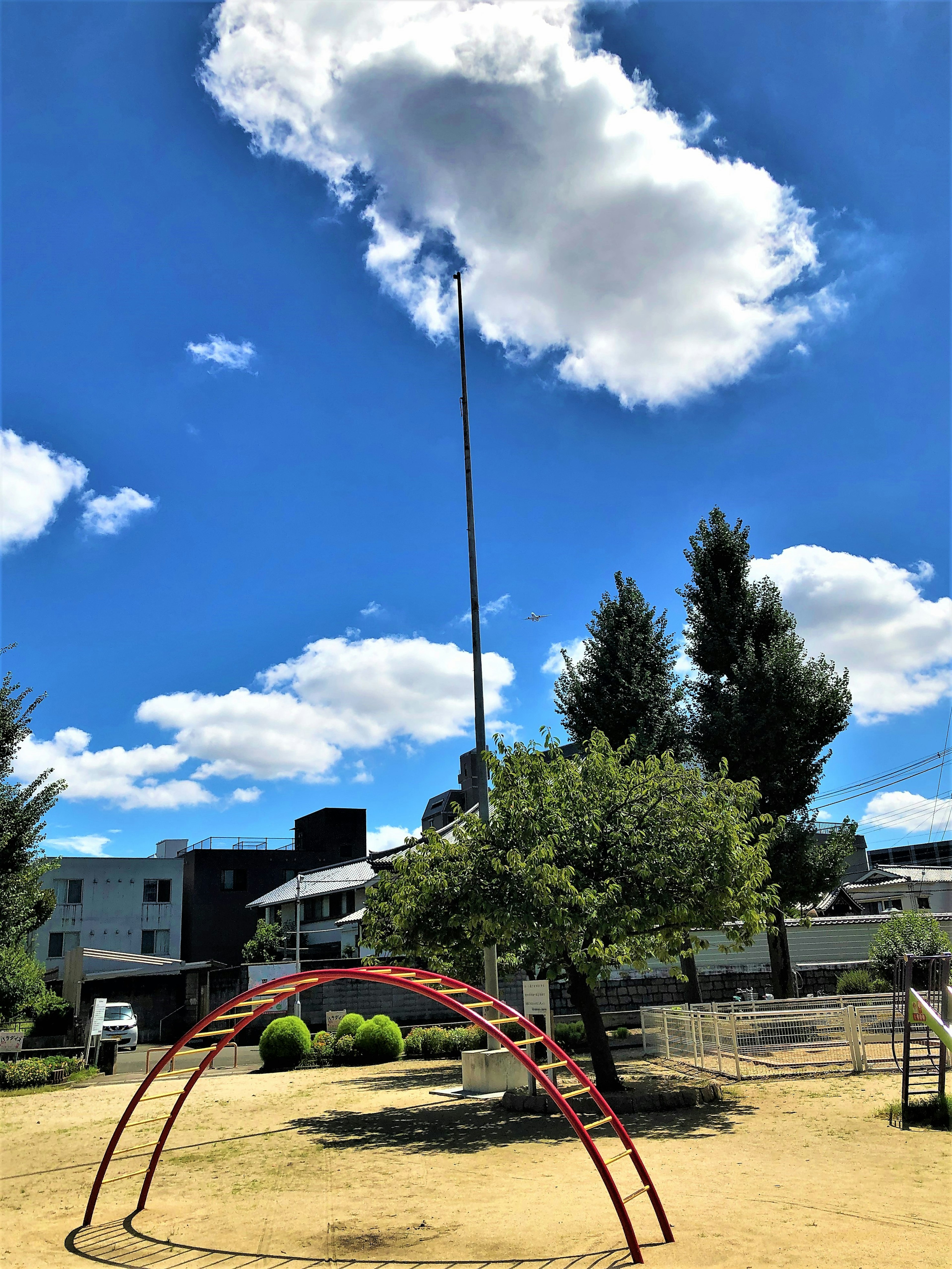 Spielplatzgeräte unter einem blauen Himmel mit Wolken und Bäumen