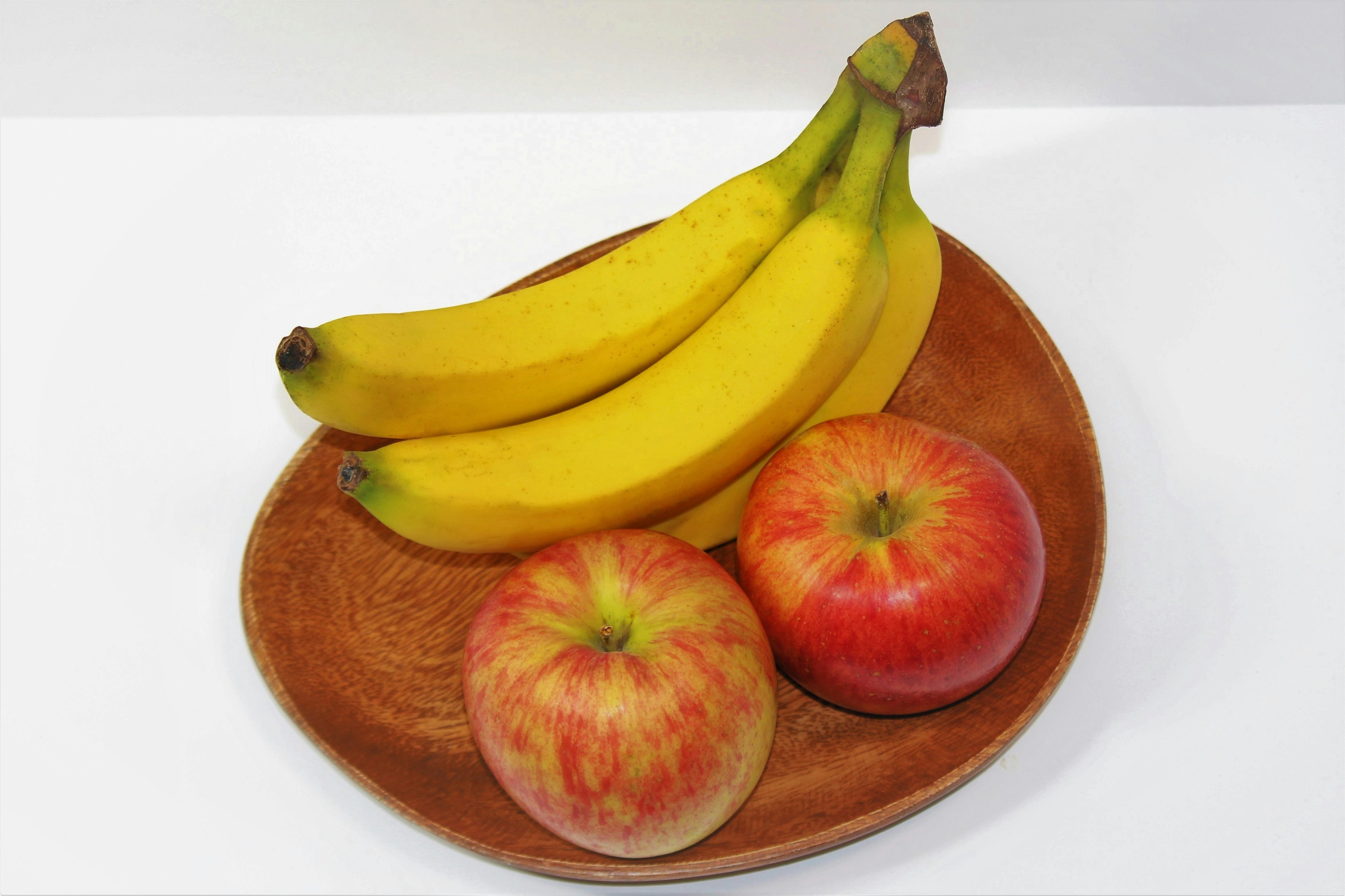 Arreglo de frutas con plátanos y manzanas en un plato de madera