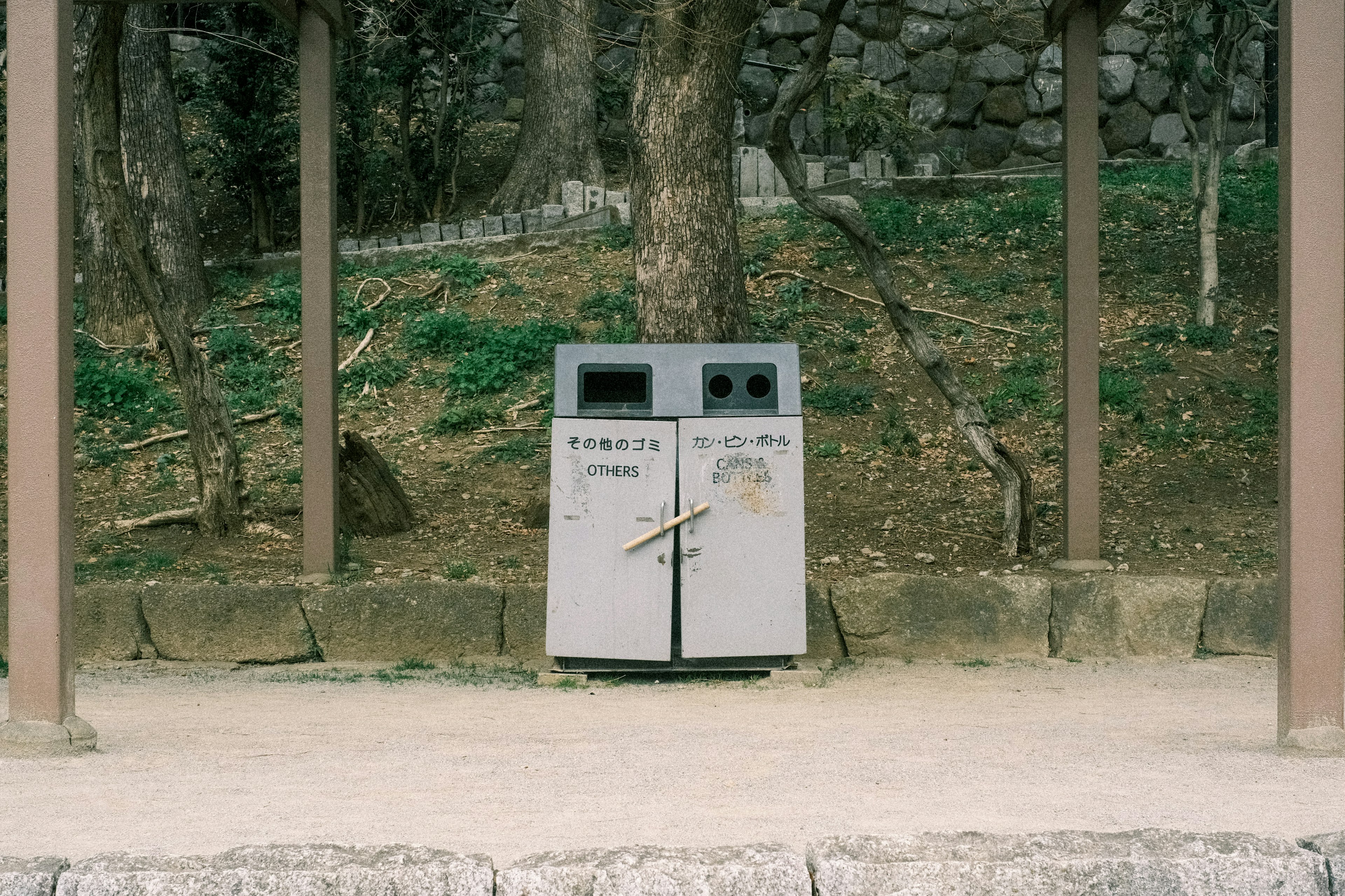 Two trash bins in a park setting surrounded by nature