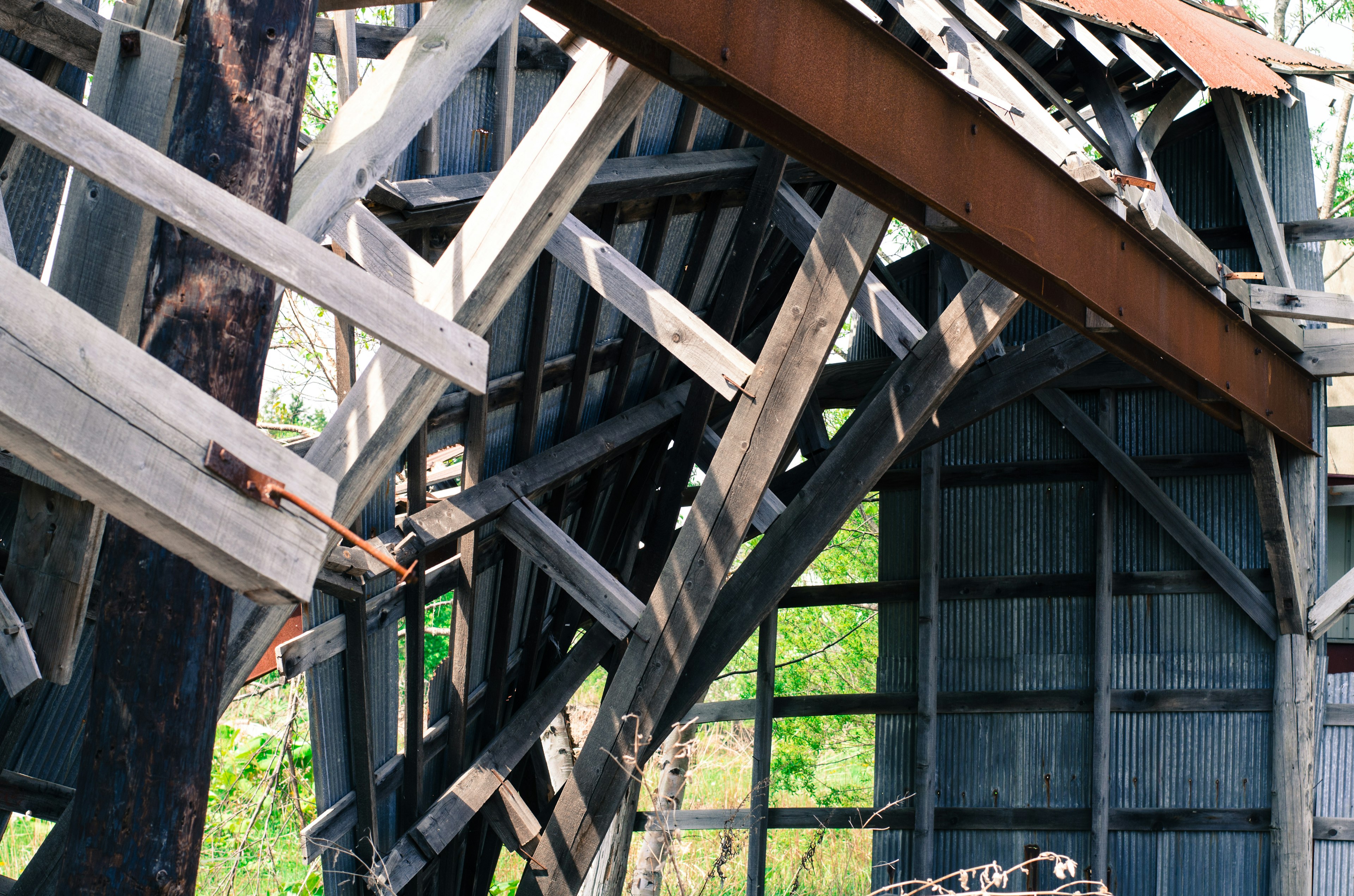 Detail interior dari struktur kayu yang bobrok dengan komponen logam berkarat dan latar belakang hijau