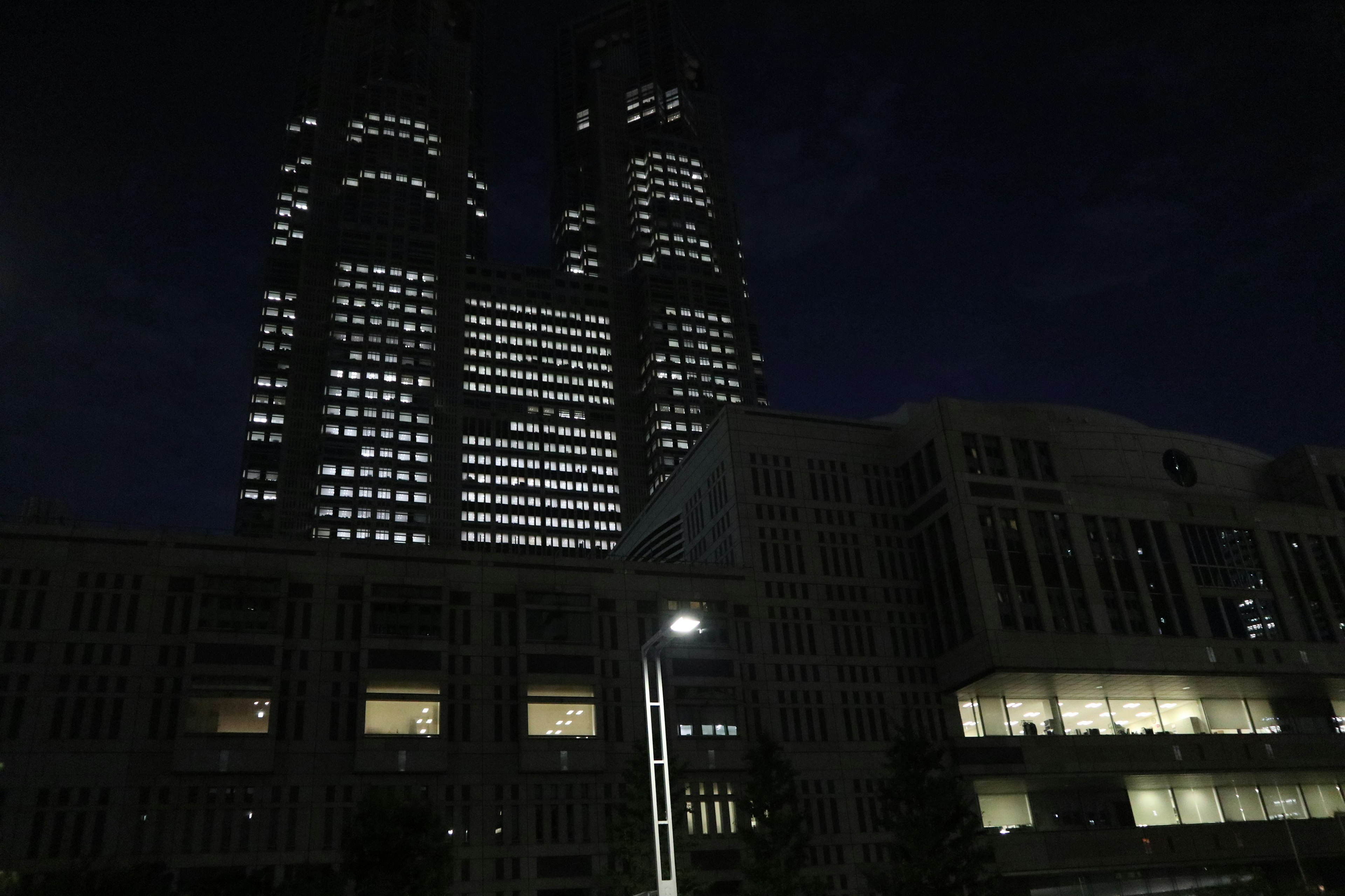 Gedung pencakar langit Tokyo di malam hari dengan menara kembar yang diterangi dari gedung pemerintah metropolitan Tokyo