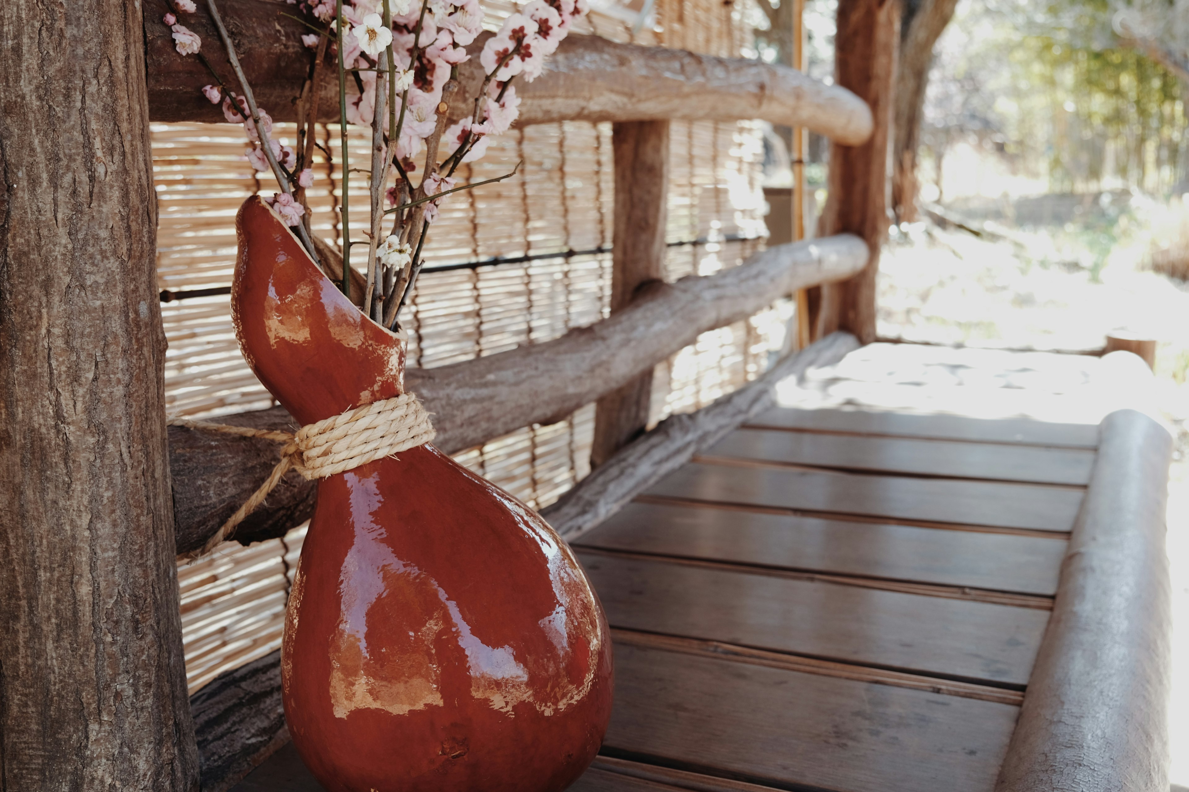 Red ceramic vase with flowers on a wooden table in a rustic setting