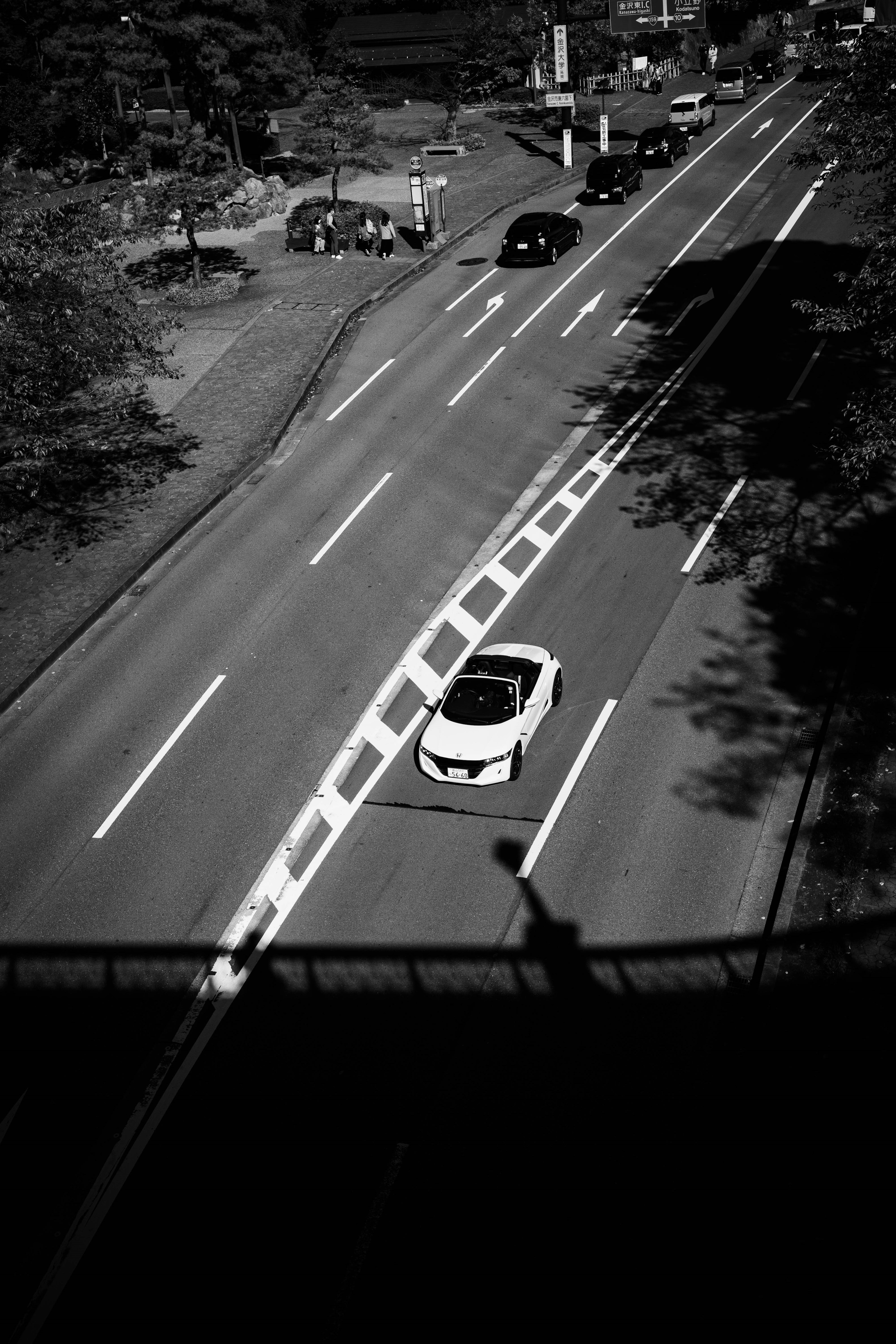 Scène de rue en noir et blanc avec une voiture et un trafic environnant