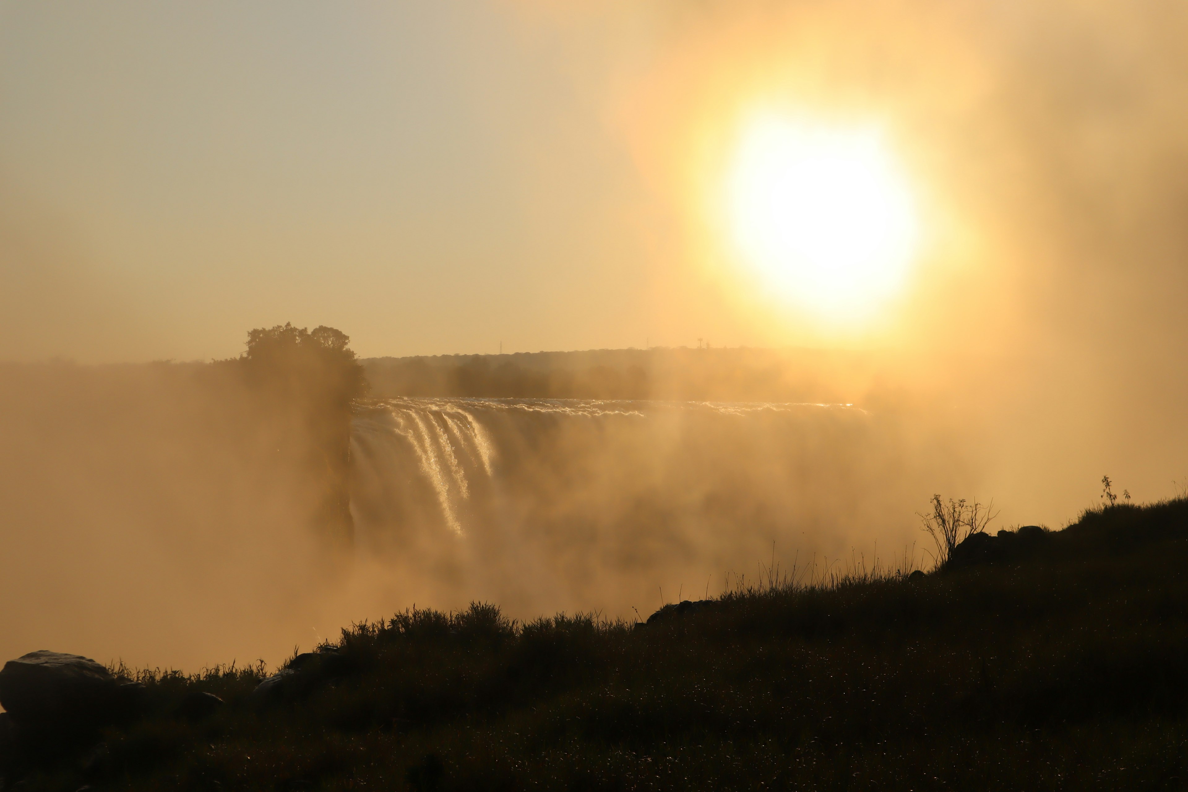 Vue du coucher de soleil derrière une cascade avec de la brume