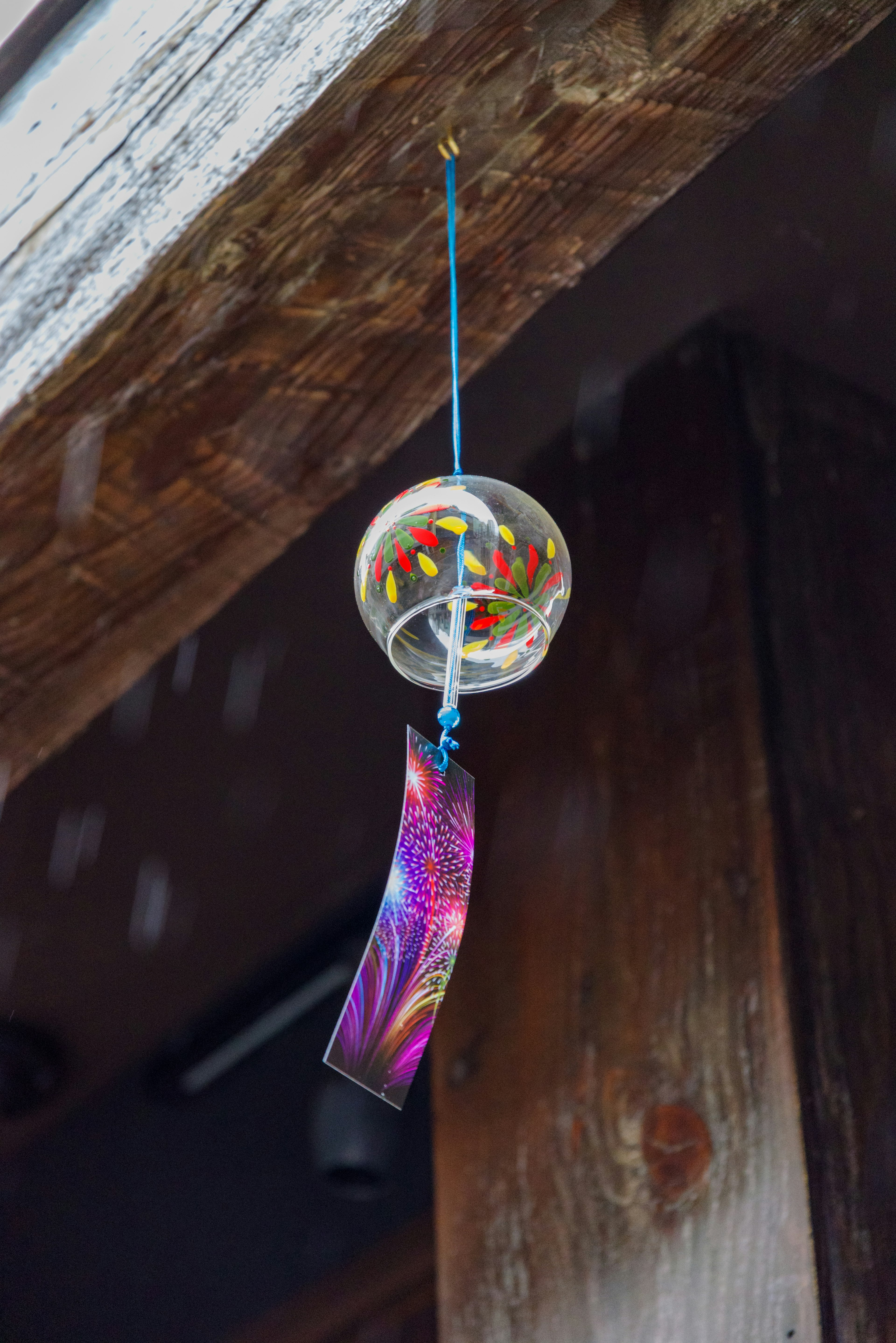 A wind chime hanging from a wooden beam featuring a transparent sphere with colorful patterns and a decorative strip below