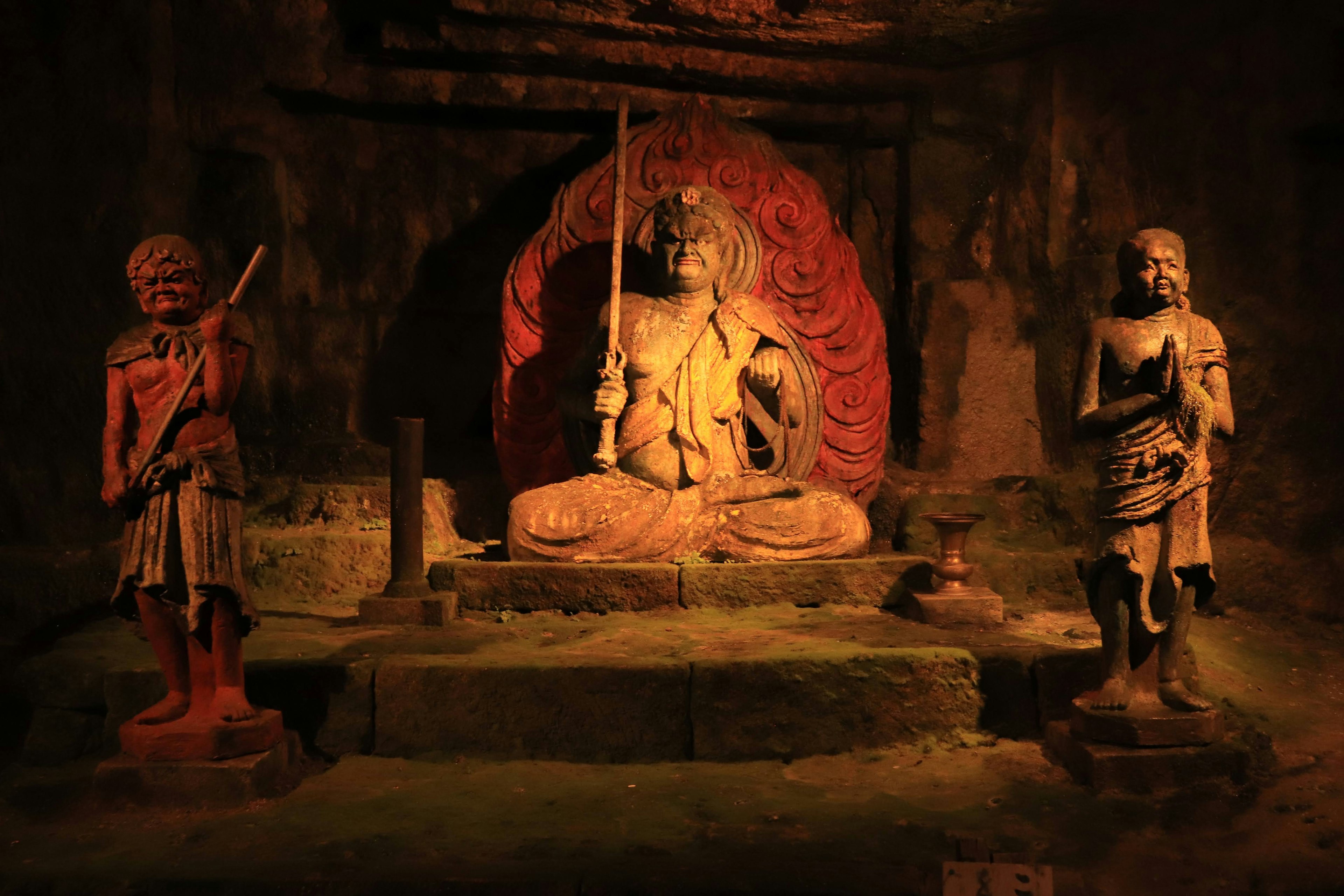 Una scena mistica con una statua di Buddha seduto e due figure guardian in una grotta