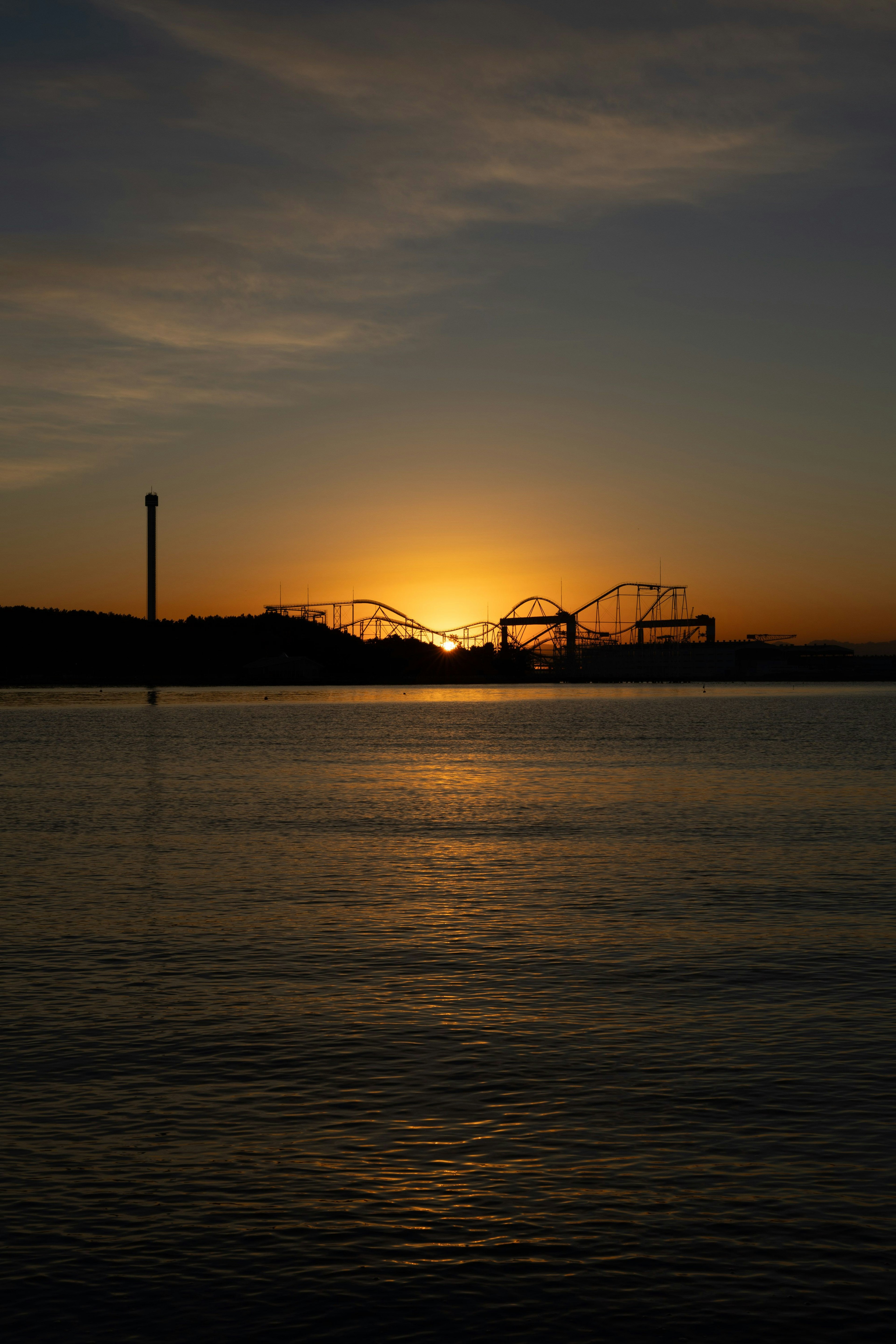 Schöner Sonnenuntergang, der sich im Wasser spiegelt, mit Riesenrad und Achterbahn in der Ferne