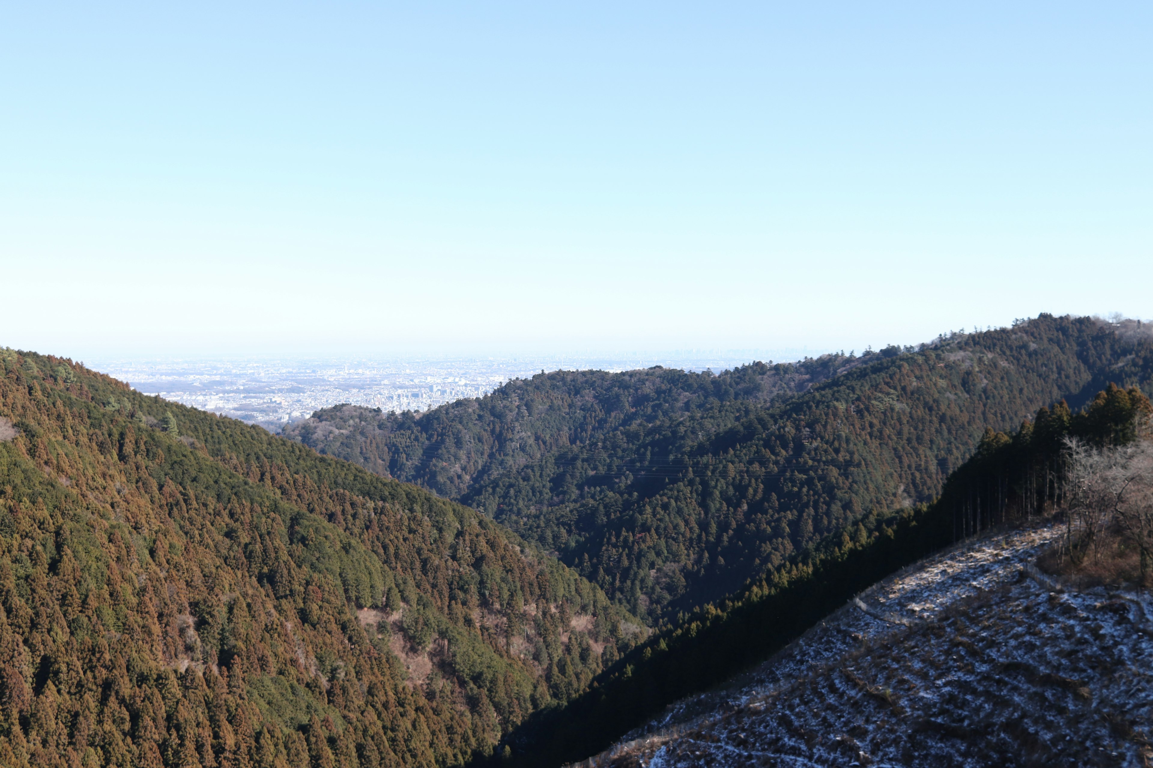 Vista panoramica di un paesaggio montano verde con macchie di neve sotto un cielo blu chiaro