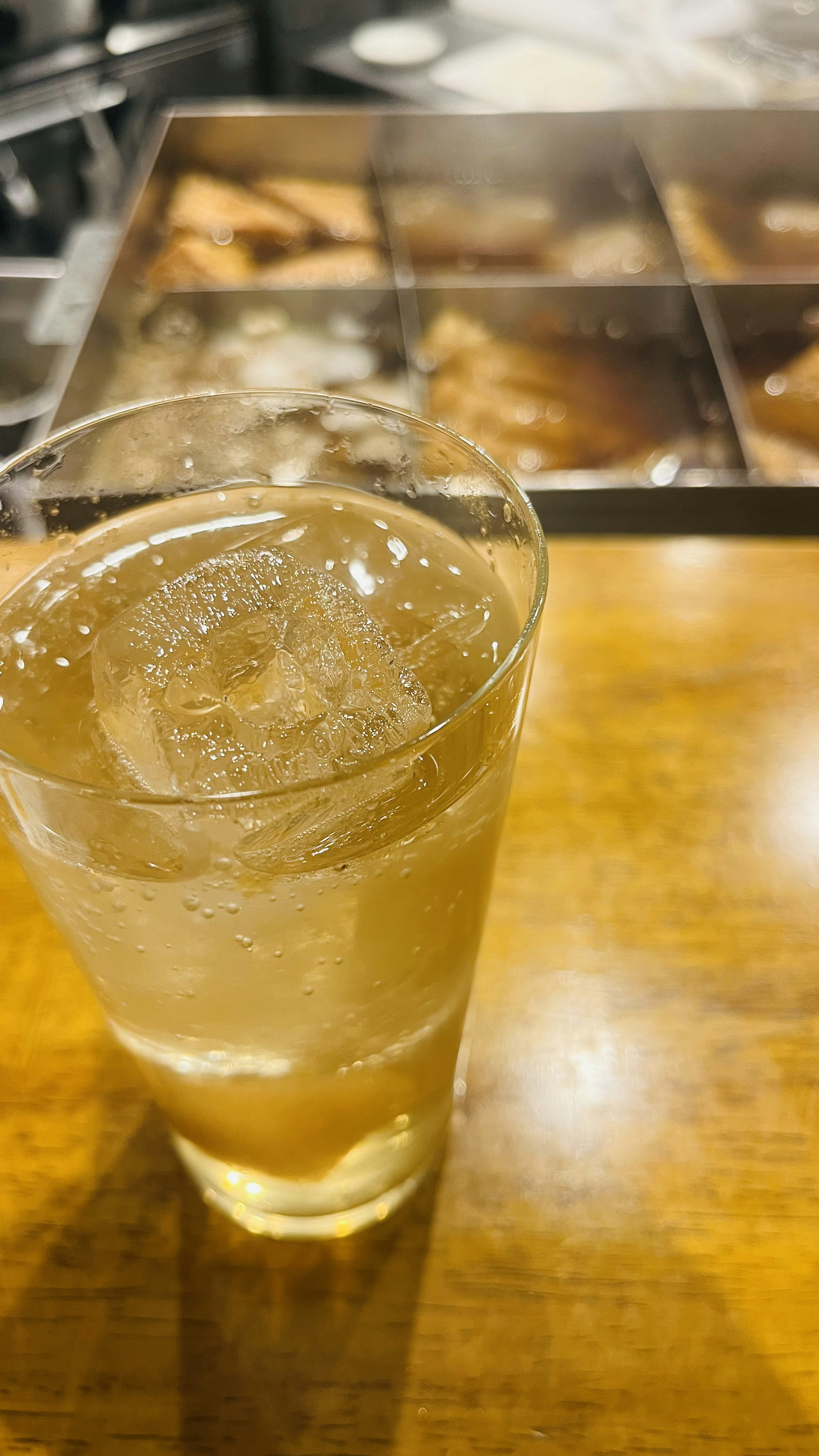 Ein Glas mit Getränk und Eis auf einem Holztisch mit verschiedenen Gerichten im Hintergrund