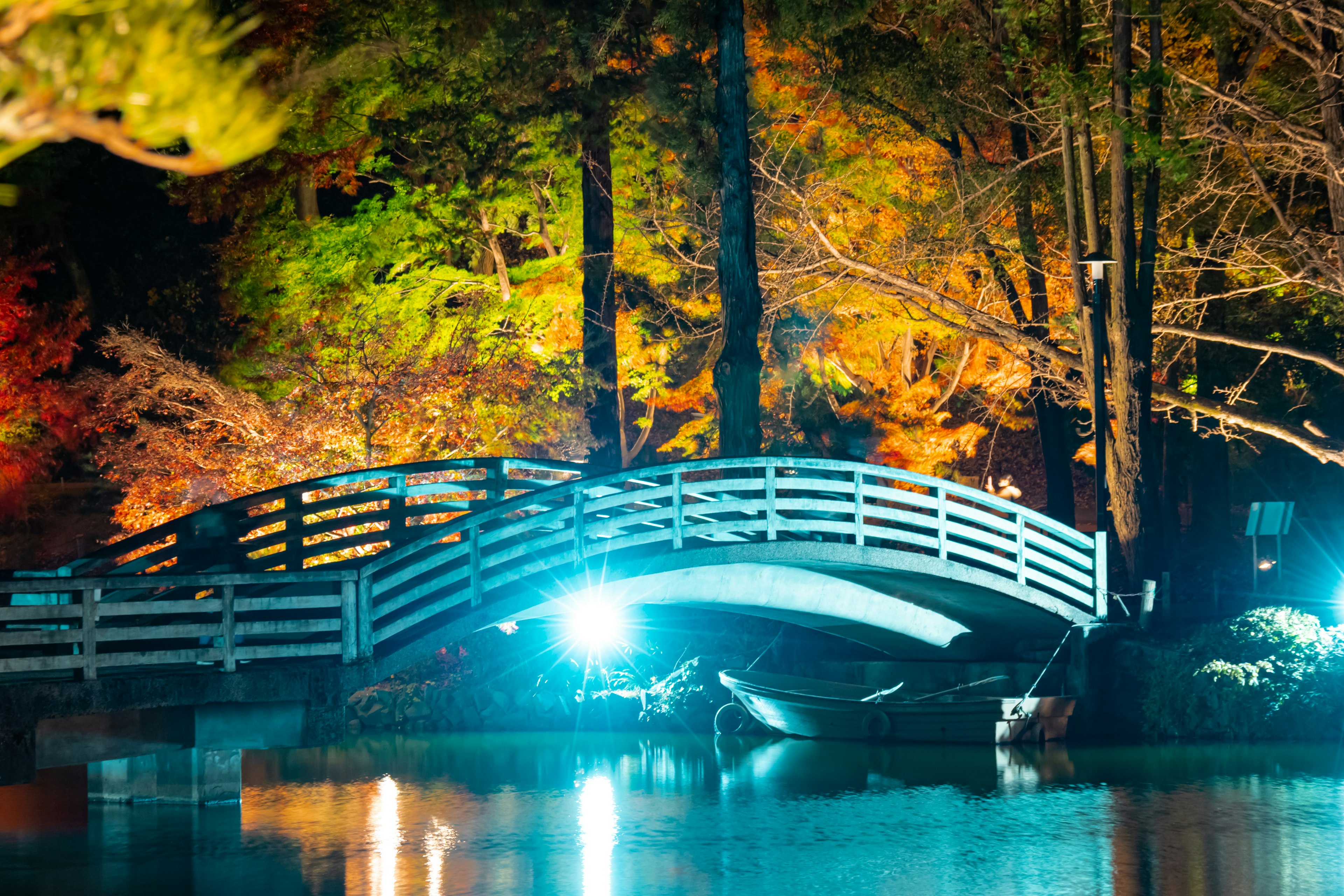 A white bridge over a tranquil lake at night surrounded by colorful trees