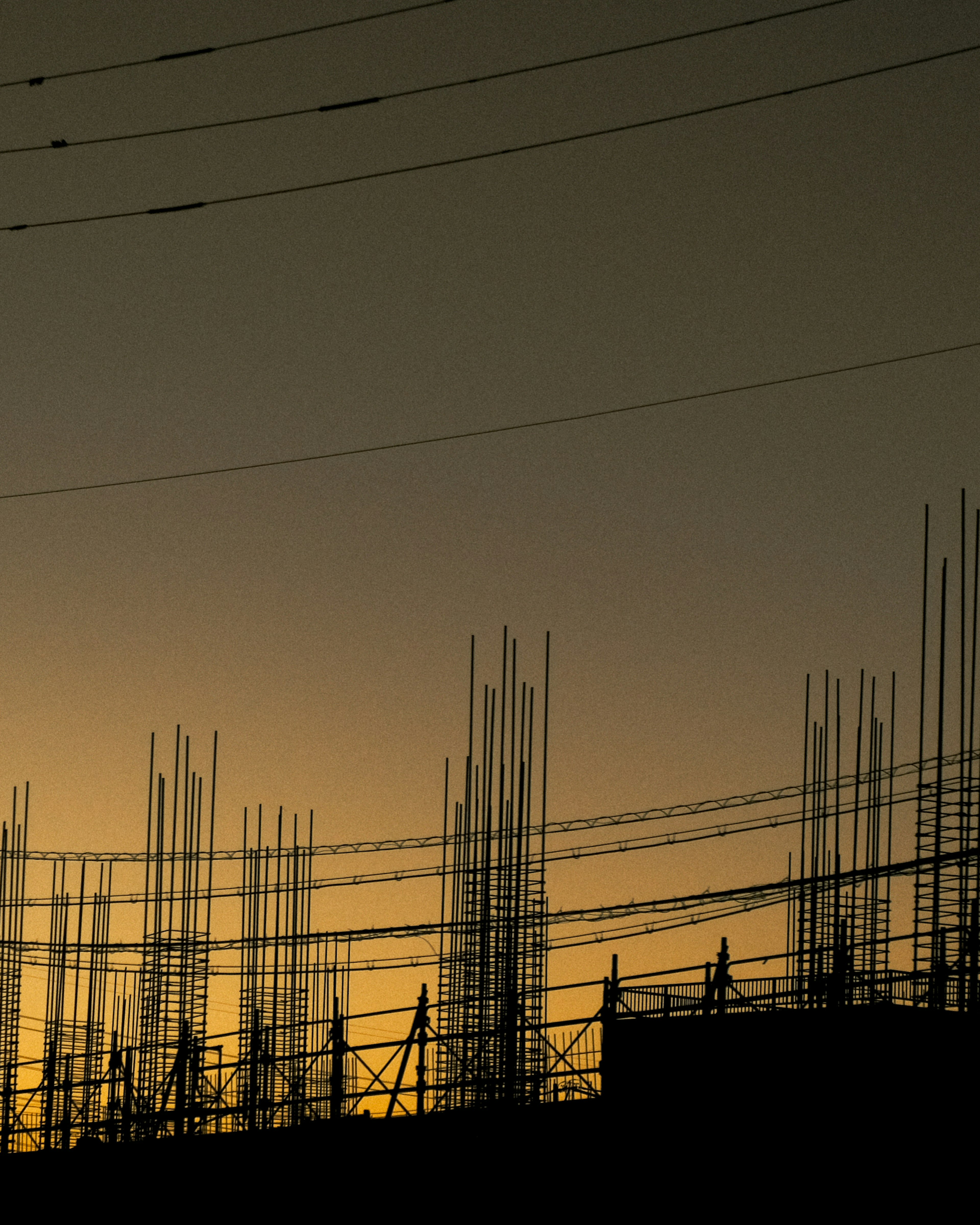 Silhouetted construction rebar and power lines against a sunset