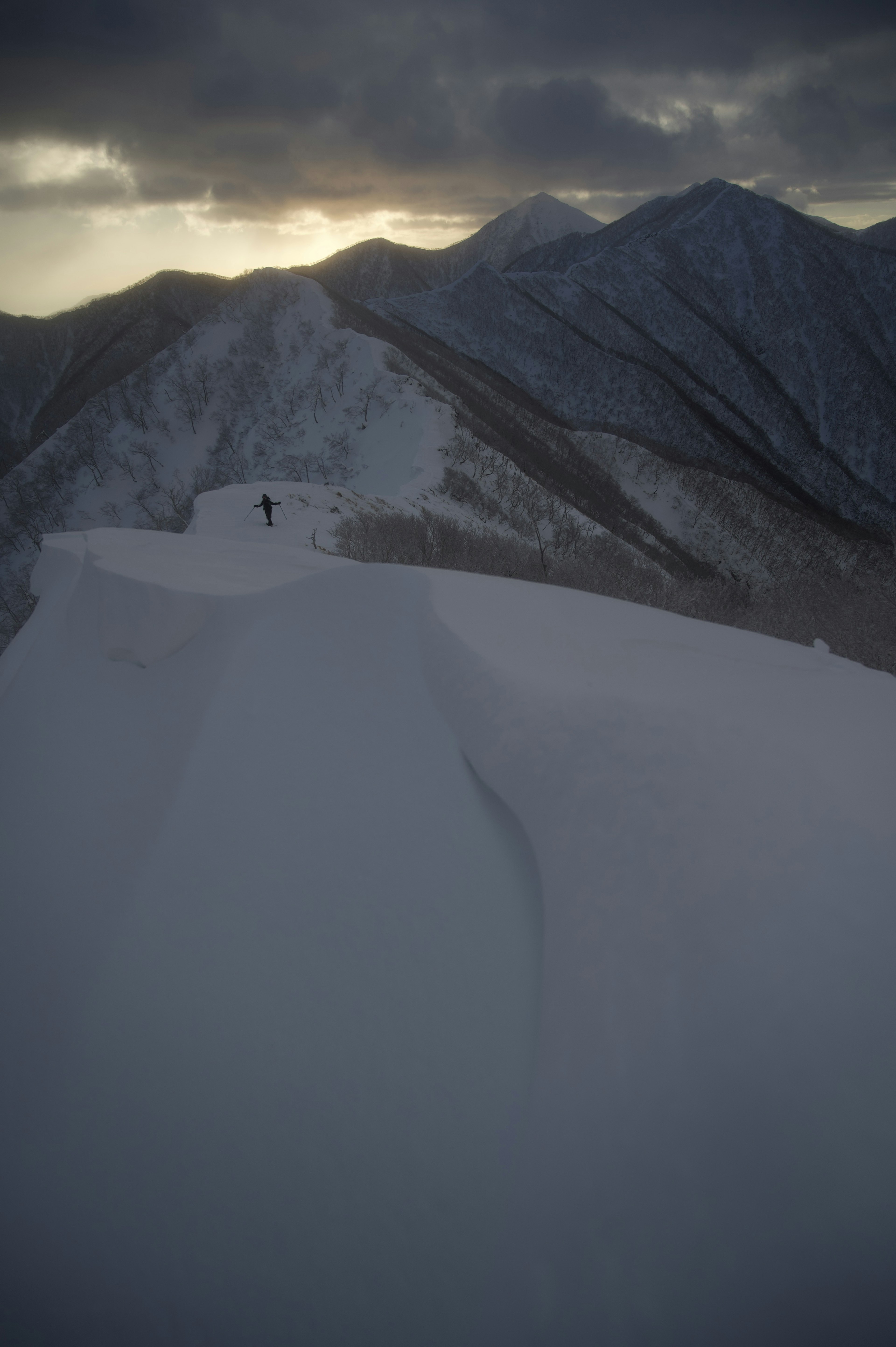 Silhouette di un alpinista su una vetta montuosa coperta di neve con nuvole scure