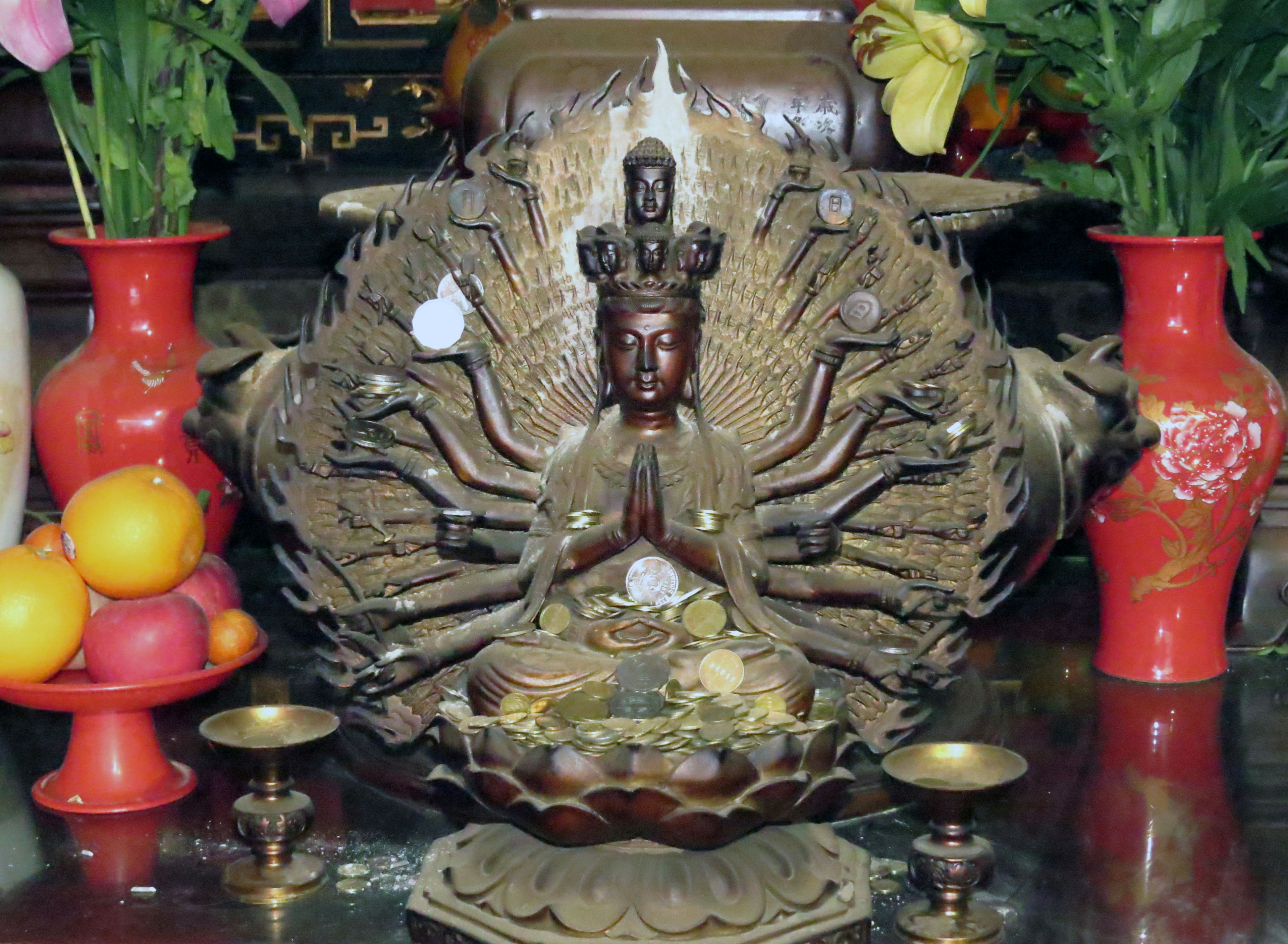 Statua multi-armata di Kannon con vasi decorativi e frutta su un altare sacro