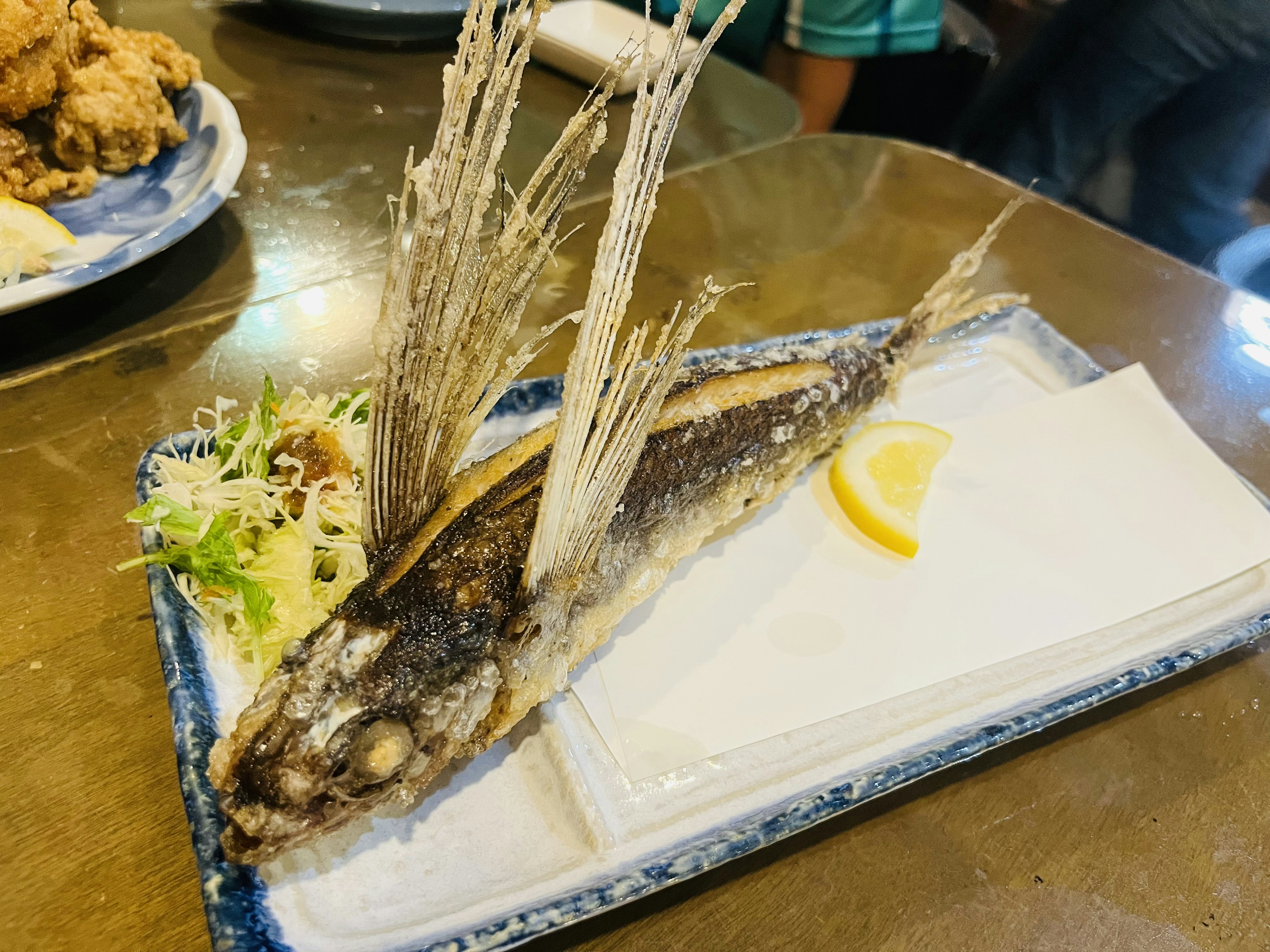 Un plat avec un poisson entier aux longues nageoires garni de citron et de salade